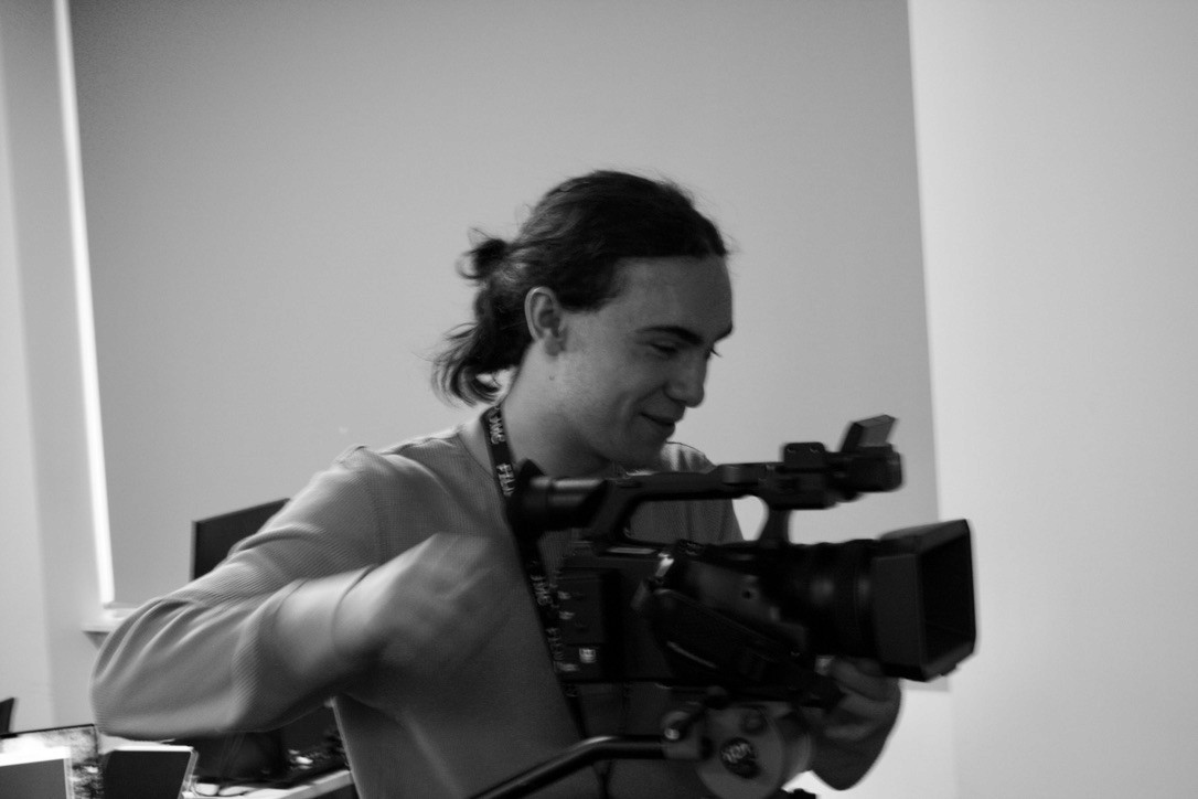 A man with a ponytail holding a video camera in a brightly lit room.