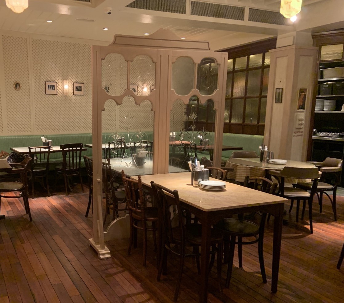 Dishoom seating. Path on left. Seating to right. Decorative glass wall beyond.