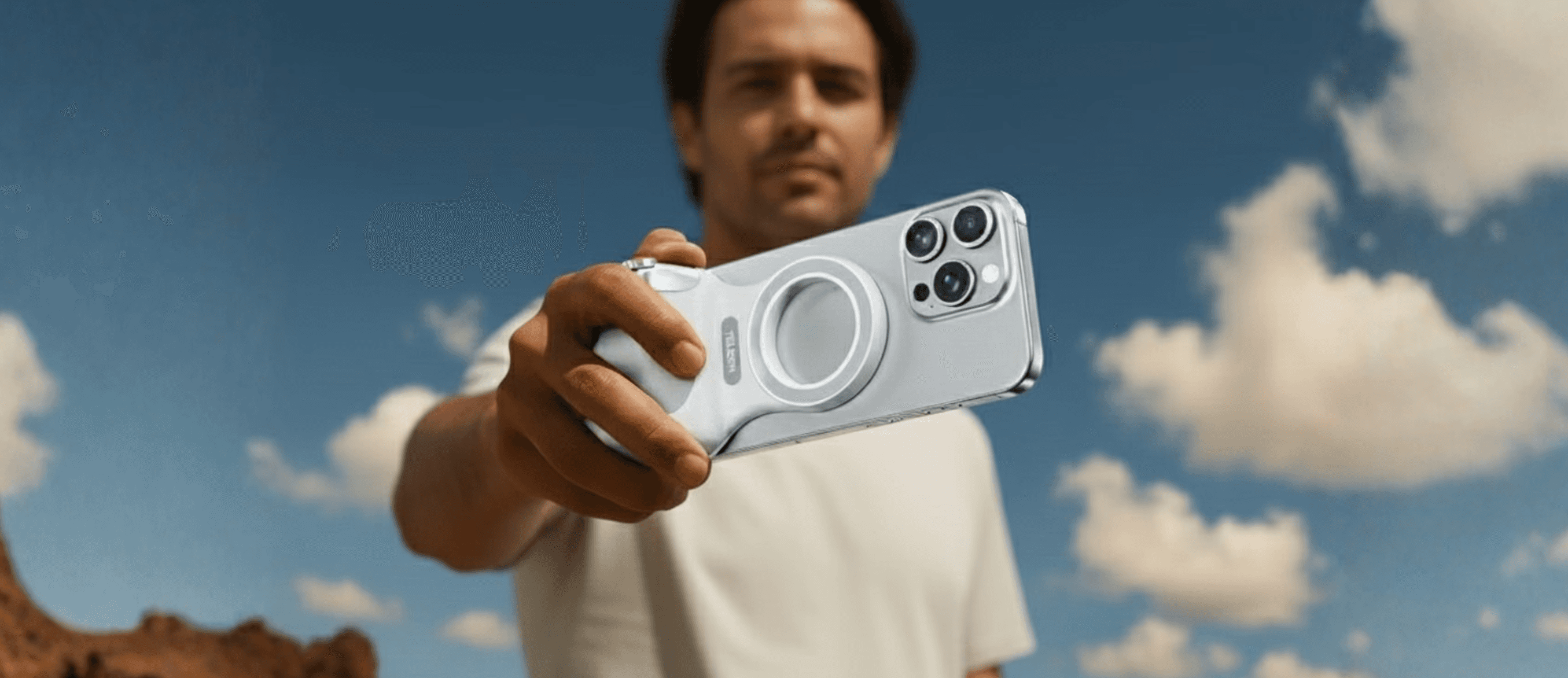 Athletic man in a sleeveless black outfit posing confidently outdoors under a bright blue sky, with a close-up of navy and salmon-colored men’s running shoes in the foreground.