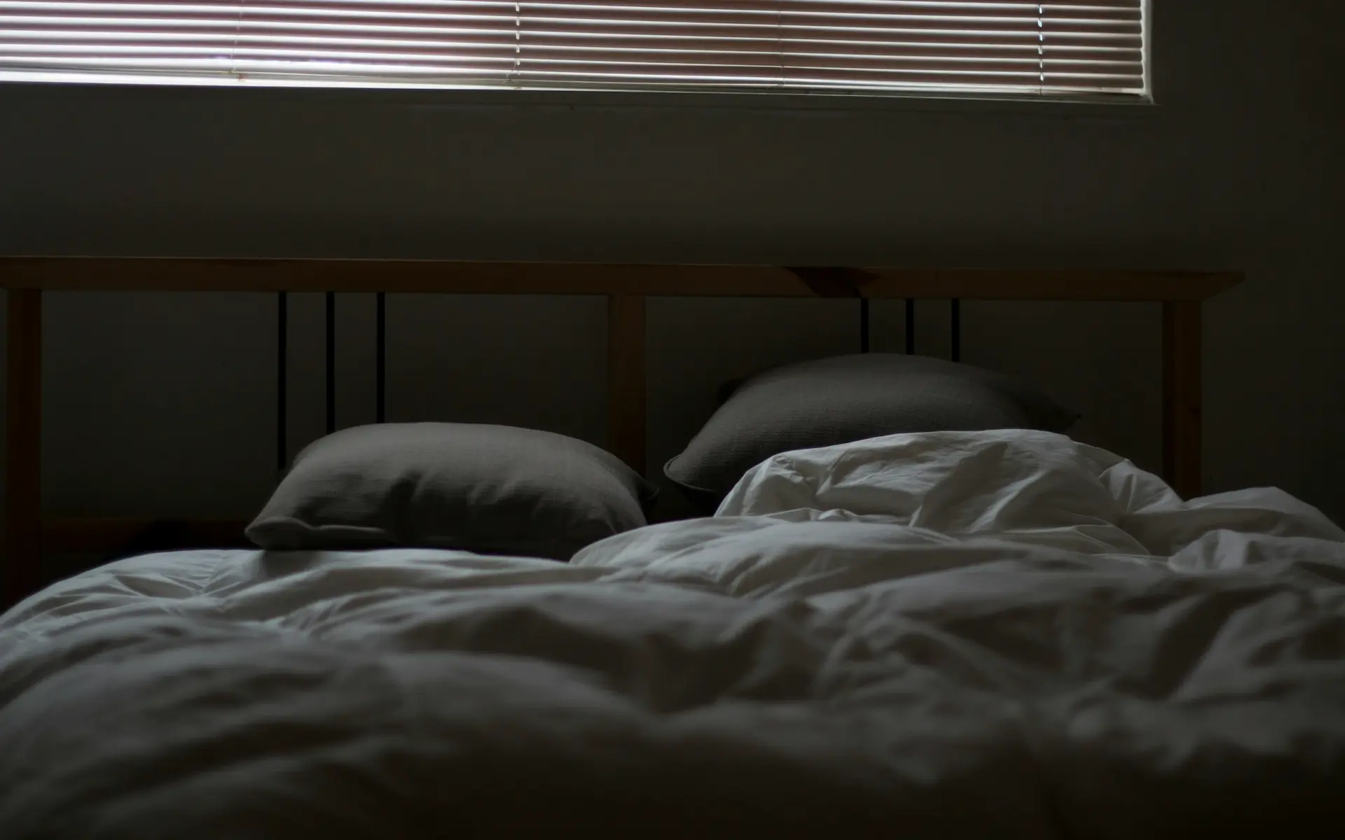 Dark bedroom with bed and pillows, blinds letting in light