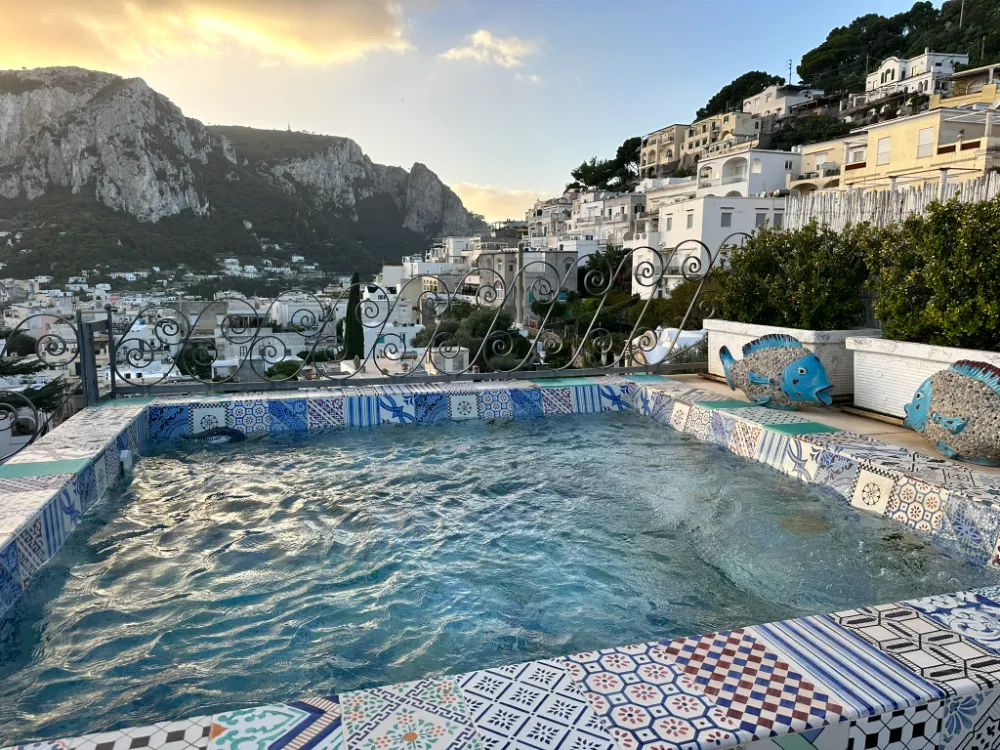 The mosaic-tiled pool at Capri Tiberio Palace, with Capri town and Monte Solaro rising behind it.