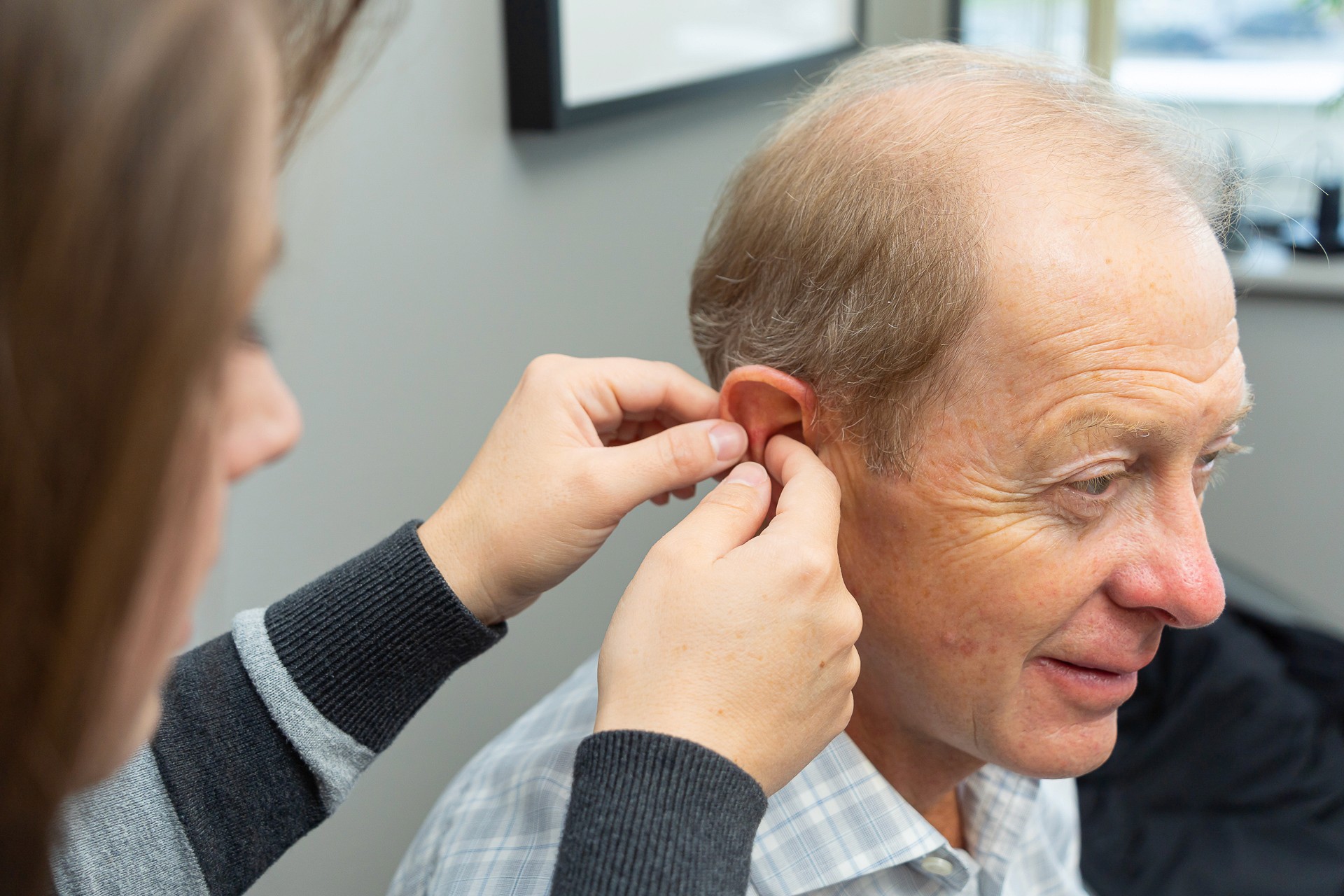 A woman helps a man by placing a hearing aid in his ear during an appointment.