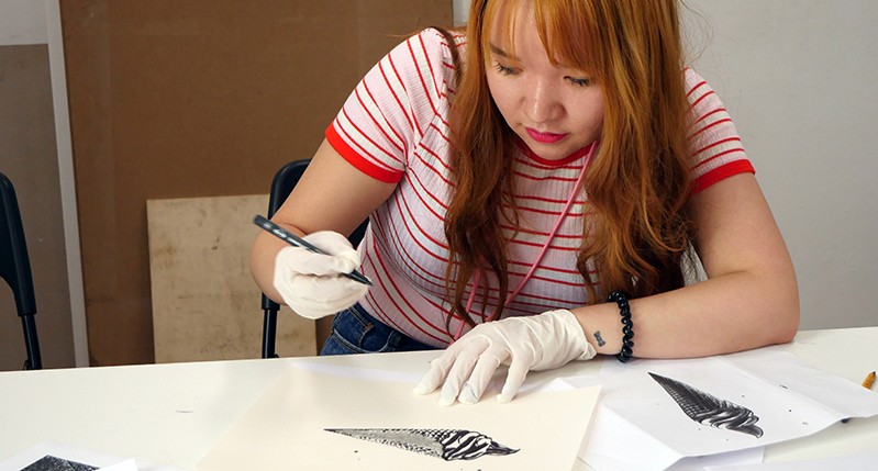 Student meticulously working on a conic seashell design on paper.