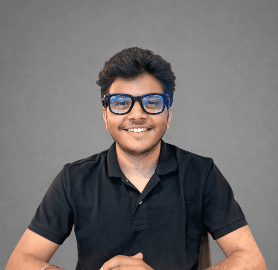 Person wearing a blue puffer jacket and red backpack standing in front of a light blue building on a city street.