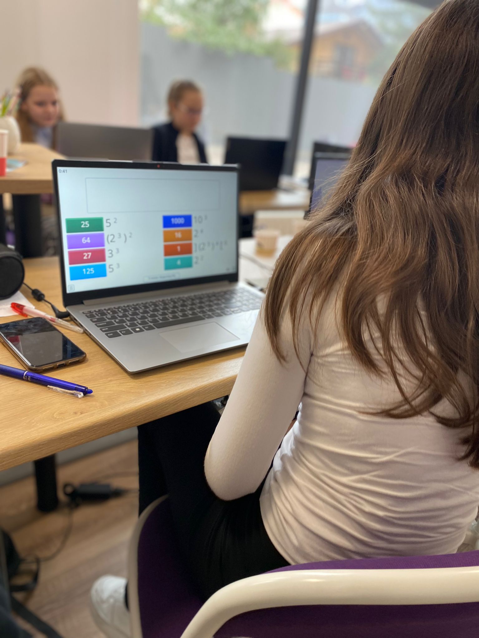 A smiling woman with her arms crossed, standing against a dark green background. She has long, dark hair.