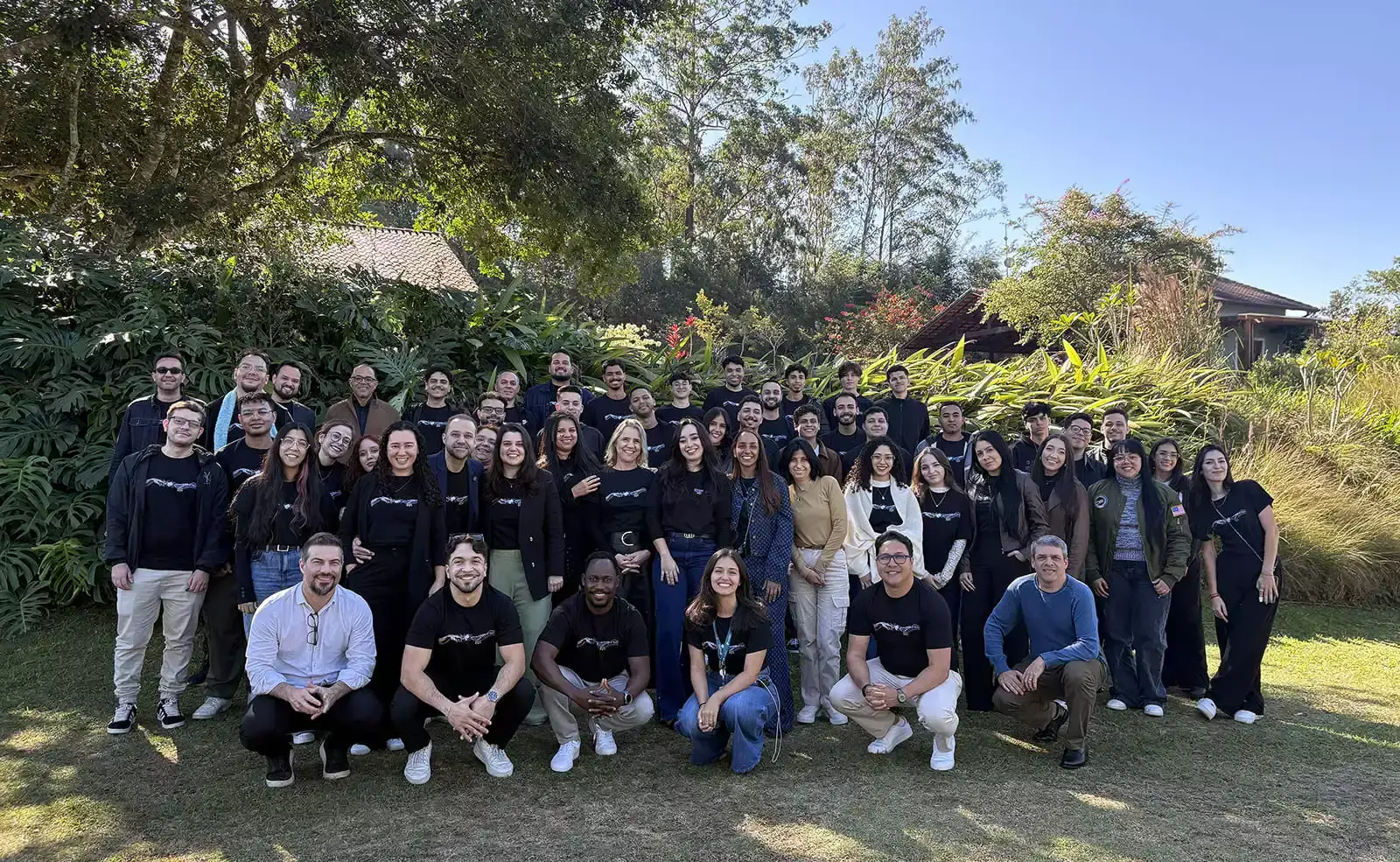 Grupo grande de pessoas sorrindo ao ar livre em frente a plantas.