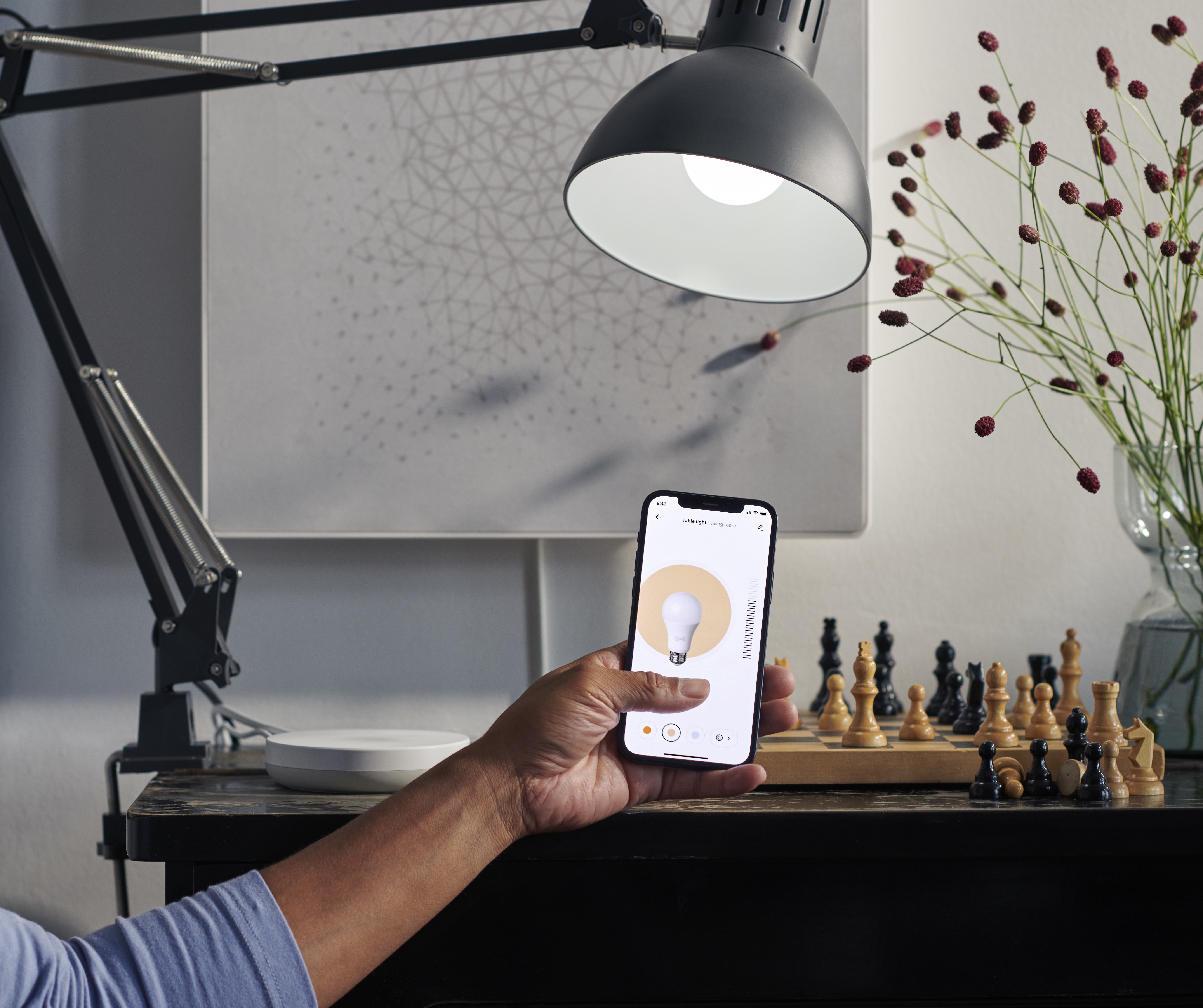 Home photo of new IKEA Home smart App in a person's hand showing the screen to adjust the light color and intensity exactly like the bulb it controls..