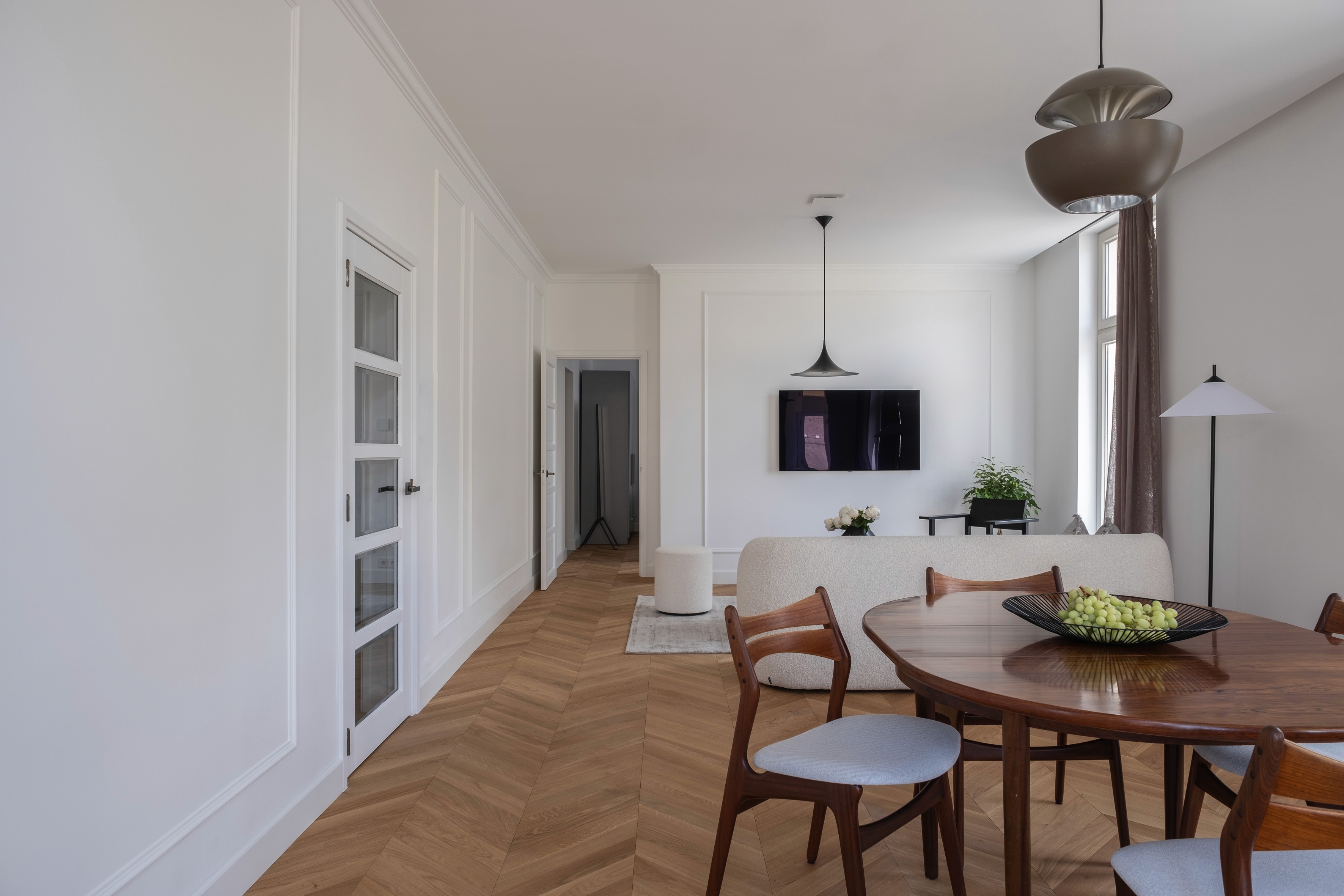 Open-plan living and dining area with Hungarian parquet flooring, Parisian-style panelled doors, black pendant light, and mid-century dining set