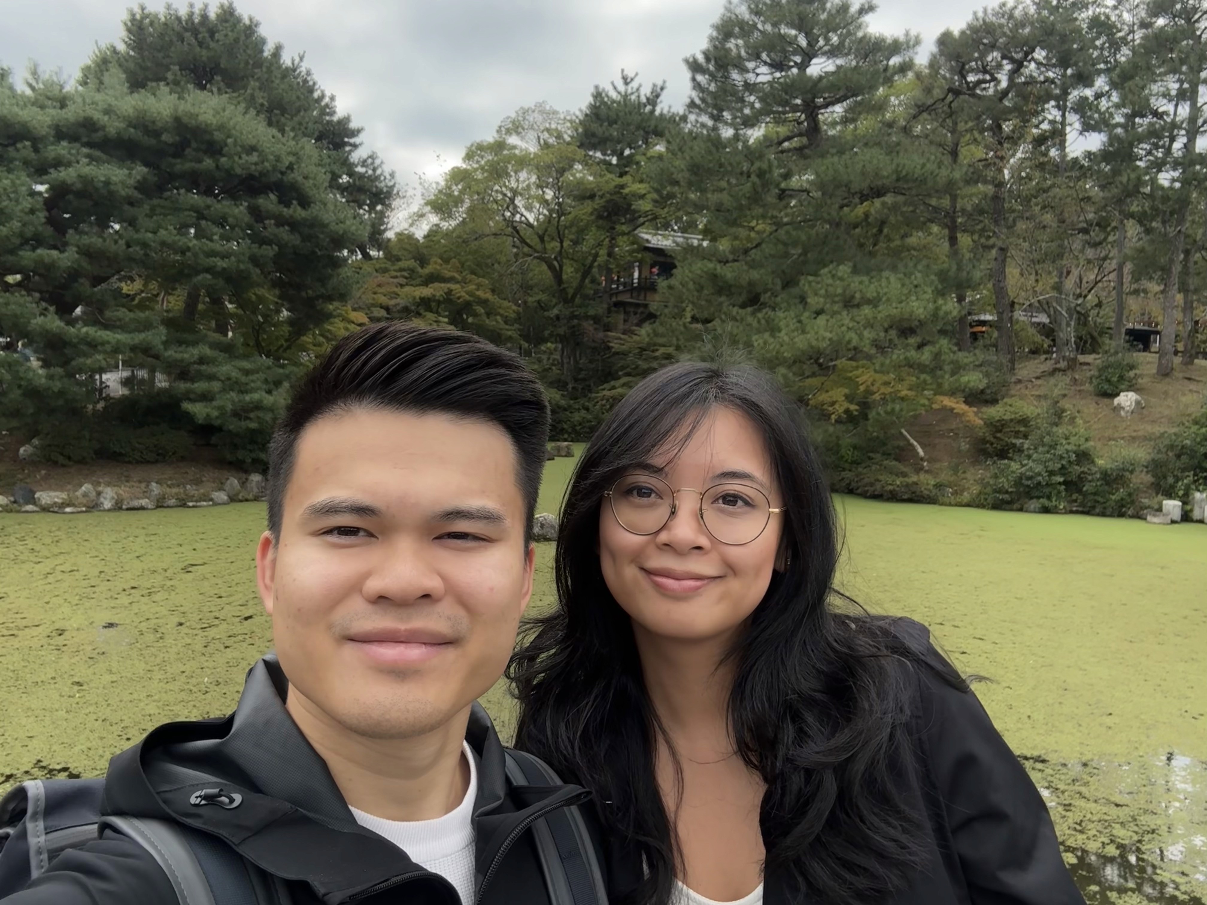 A bride and groom hold hands tenderly, the bride's bouquet of dried flowers hanging low. They stand in a softly lit, elegant interior, conveying romance.