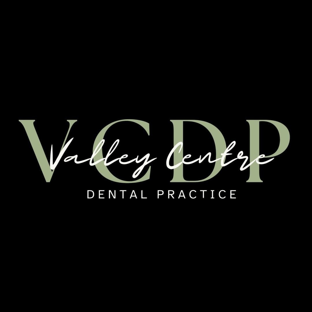 Young person with wavy hair poses confidently in sunlight against a modern building backdrop. Wears a black blazer and silver necklace, conveying elegance.