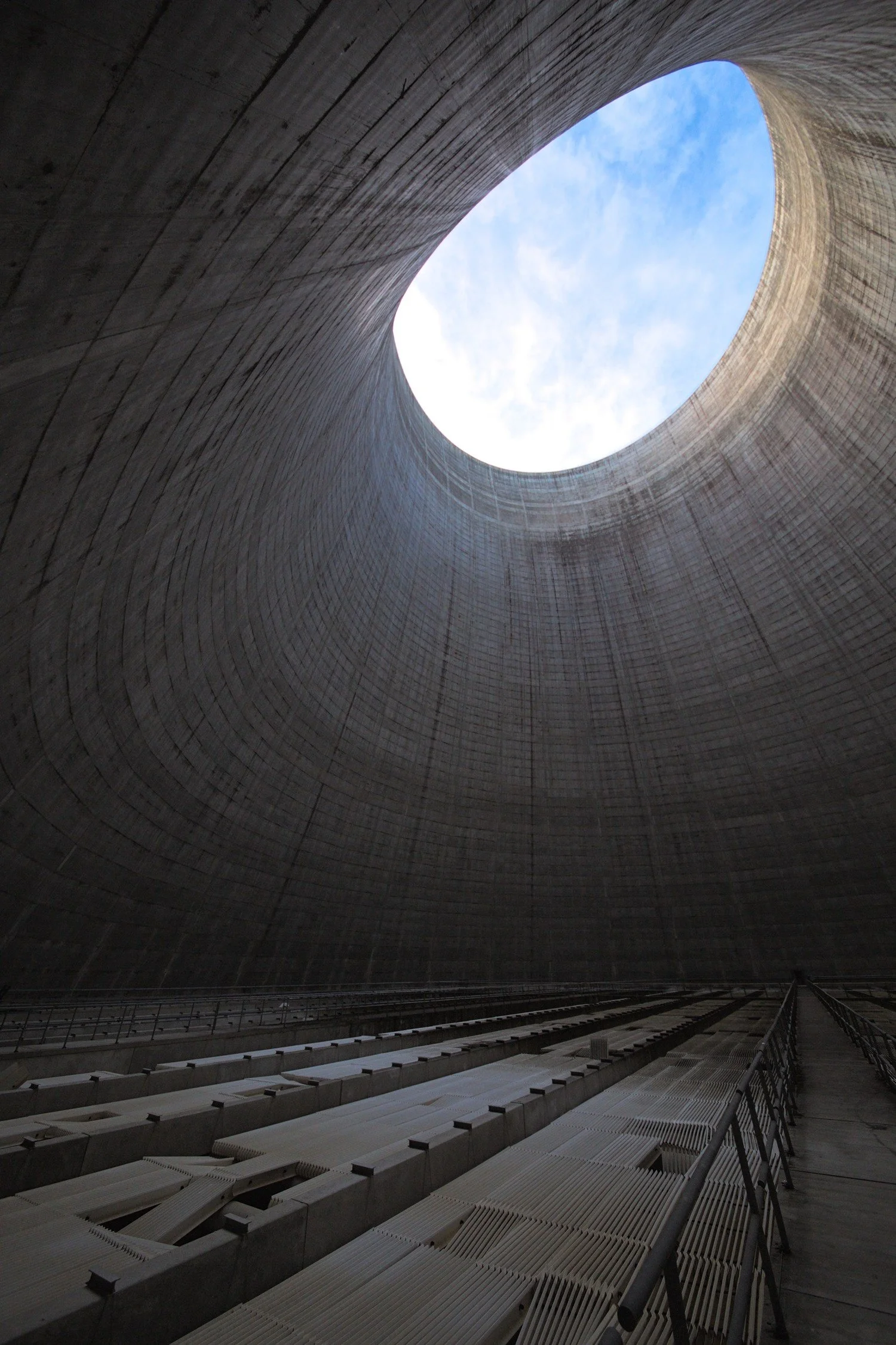 Inside a concrete cooling tower looking up toward an oval opening of sky.