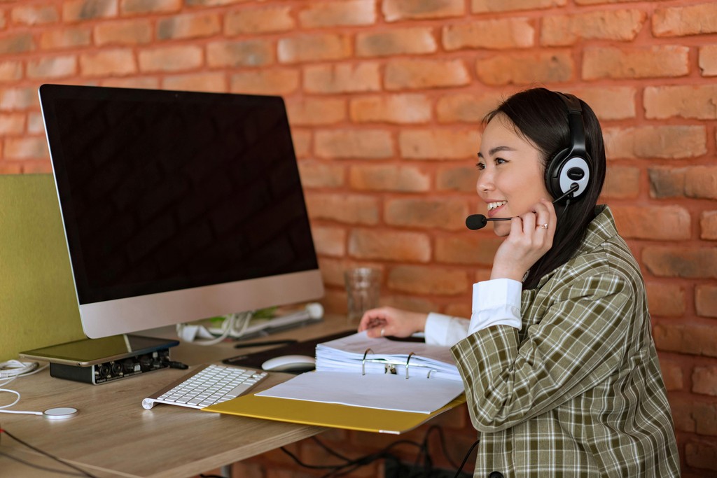 A smiling newcomer to Canada wearing a headset while working at a computer desk, representing an administrative or technical role classified under the skilled TEER categories (0, 1, 2, or 3) that qualify for Canadian Permanent Residency (PR) through Express Entry.
