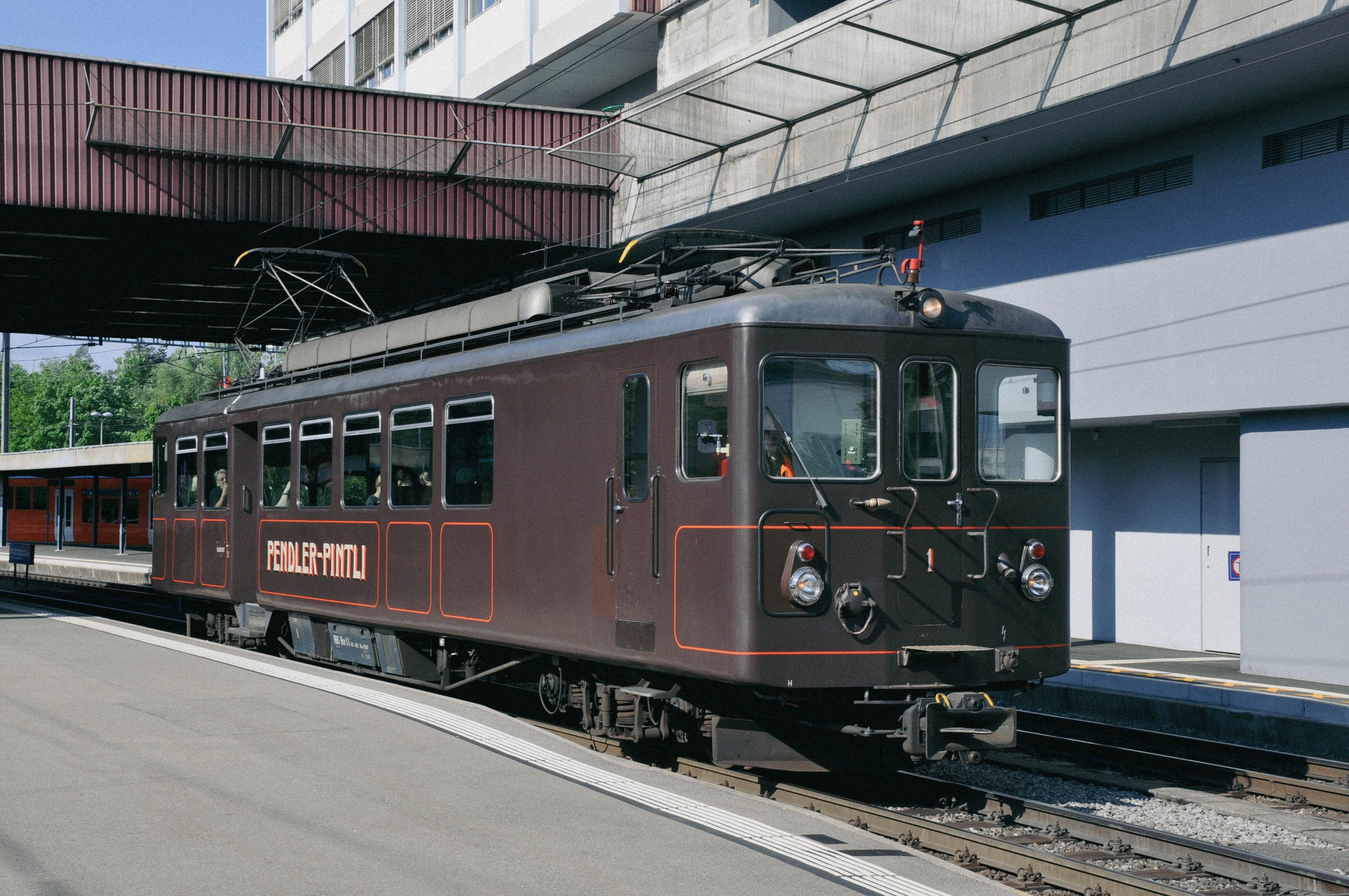 Der braune Triebzug Pendler Pintli an einem Bahnhofperron vom RBS