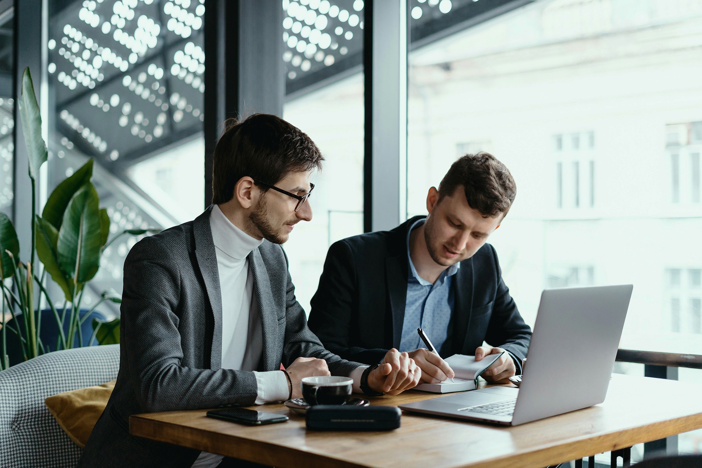 Two professional men in conversation at a desk with a laptop in fron of them