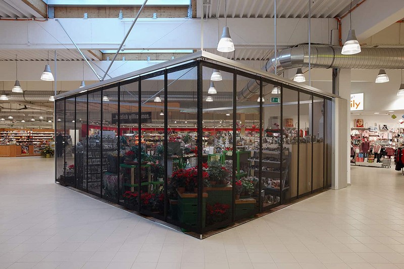 Flower shop enclosure inside a brightly lit store, offering various plants and floral arrangements.