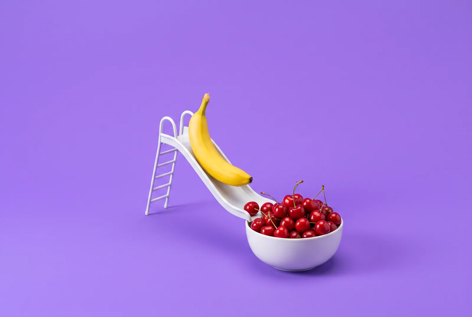 A banana sliding down a tiny slide into a bowl of cherries, when a husband looking at other women online slides into porn