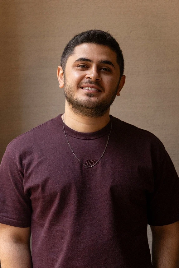 Half-length portrait in a burgundy t-shirt, neutral wall background, soft indoor light.