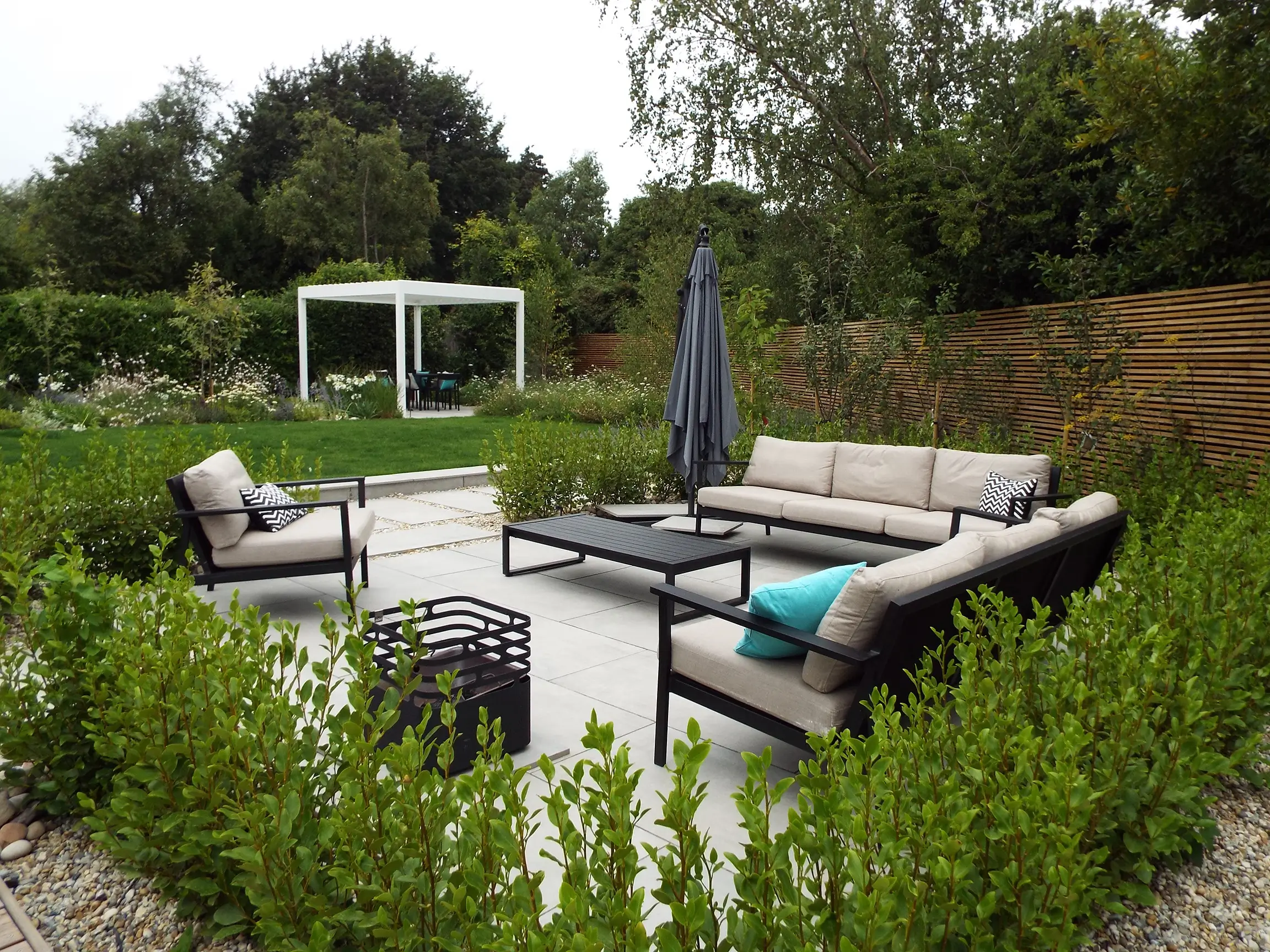 Modern outdoor seating area surrounded by greenery, featuring a fire pit and a small pool.