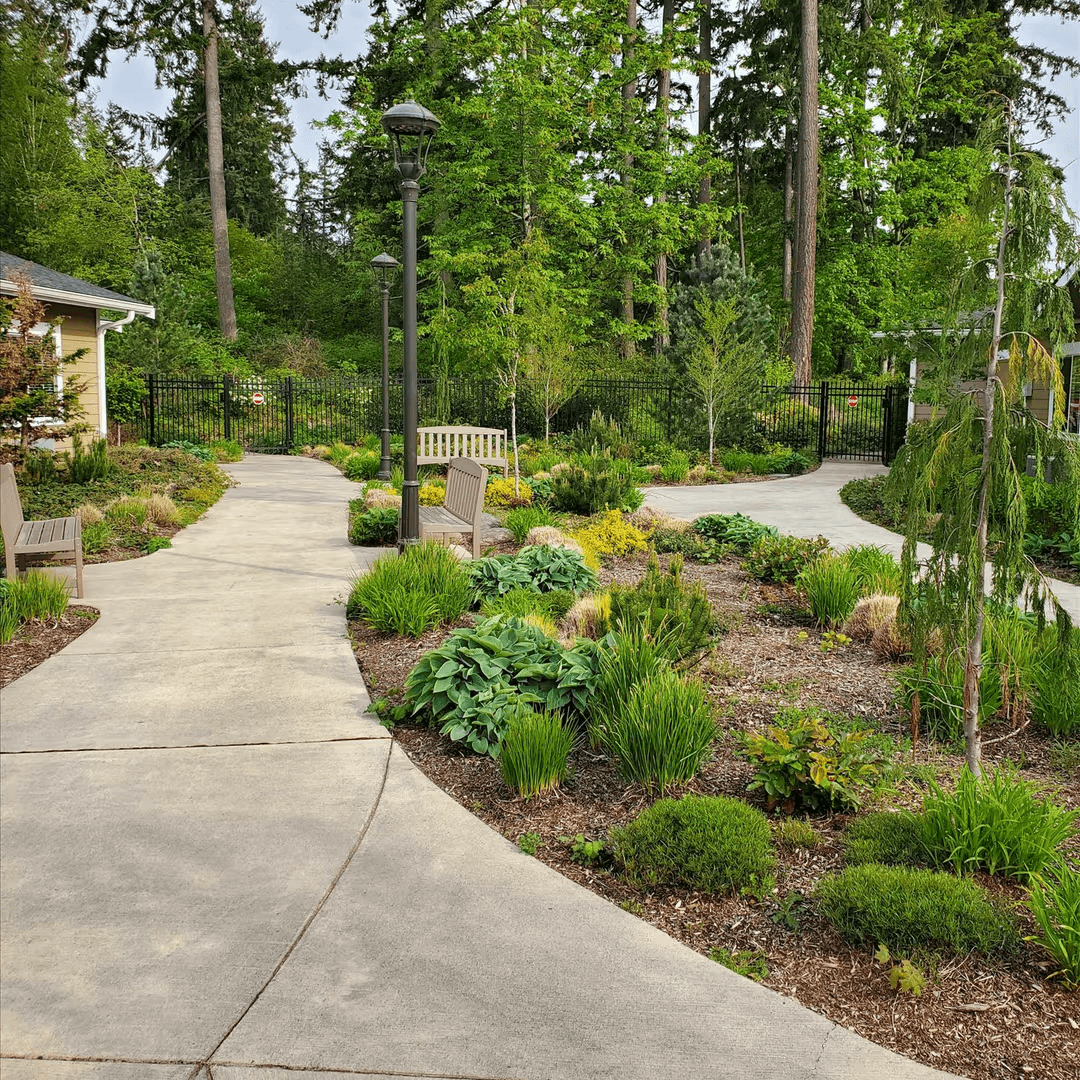 Secure outdoor walking path with paved trails and fencing for residents in a memory care community.