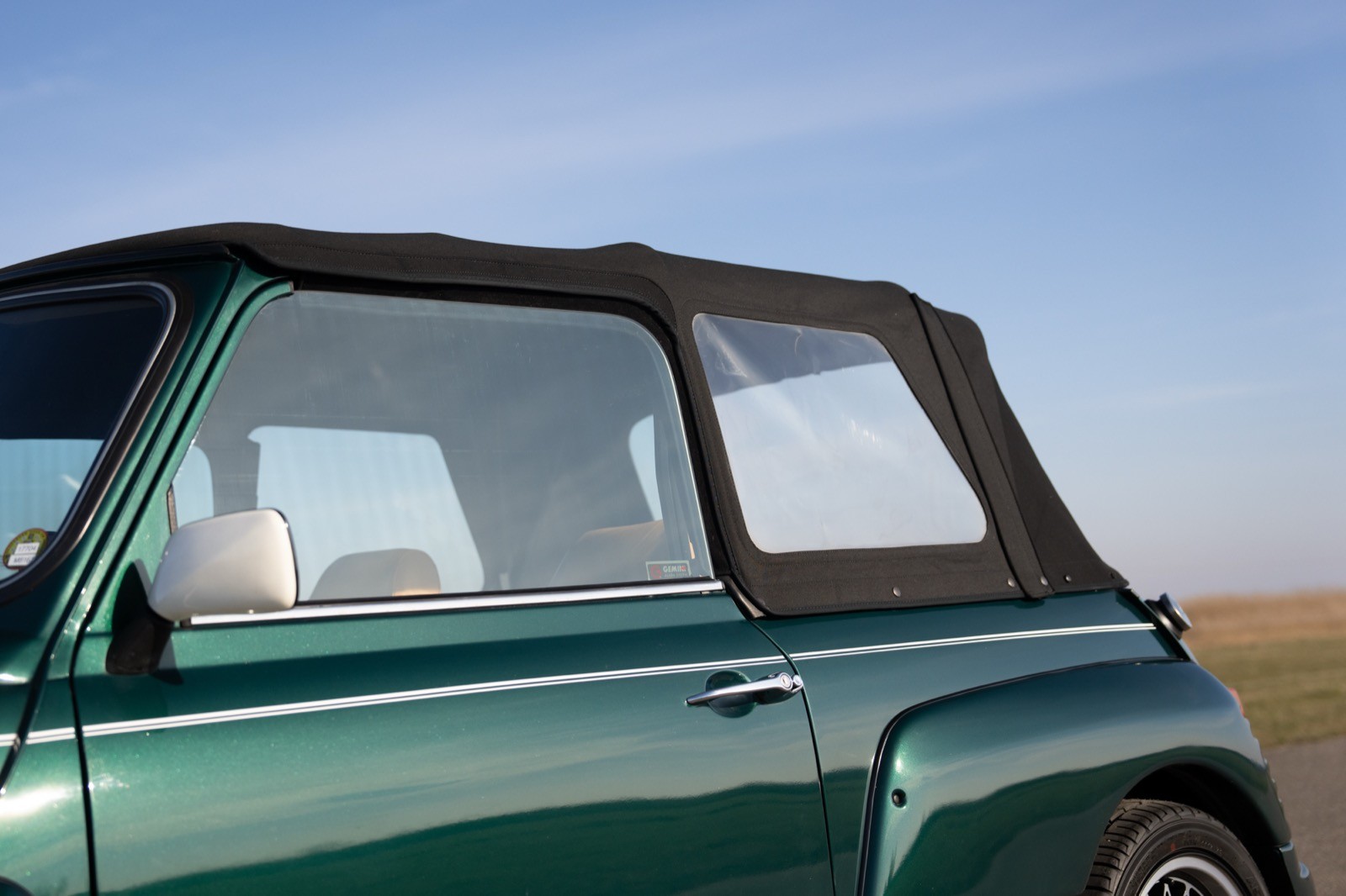 Close-up of the side of a green convertible car showing a soft top, with a clear sky in the background.