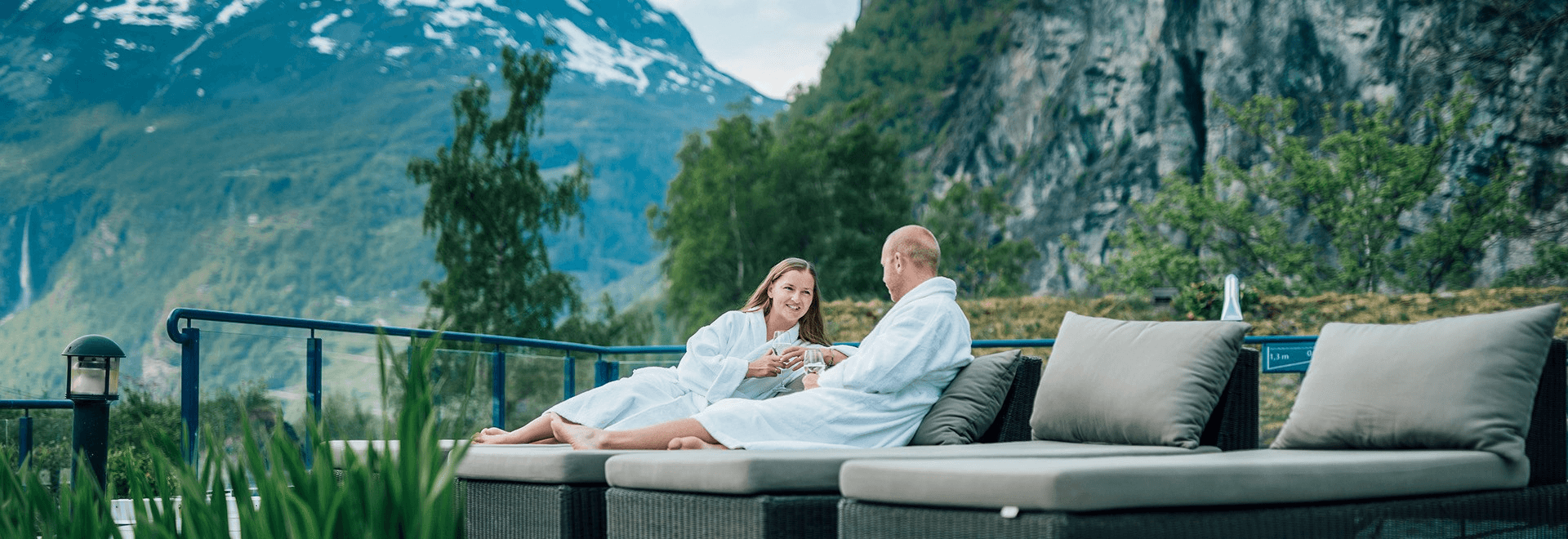 Two people relax on a sofa in a scenic outdoor setting, surrounded by mountains and lush greenery.