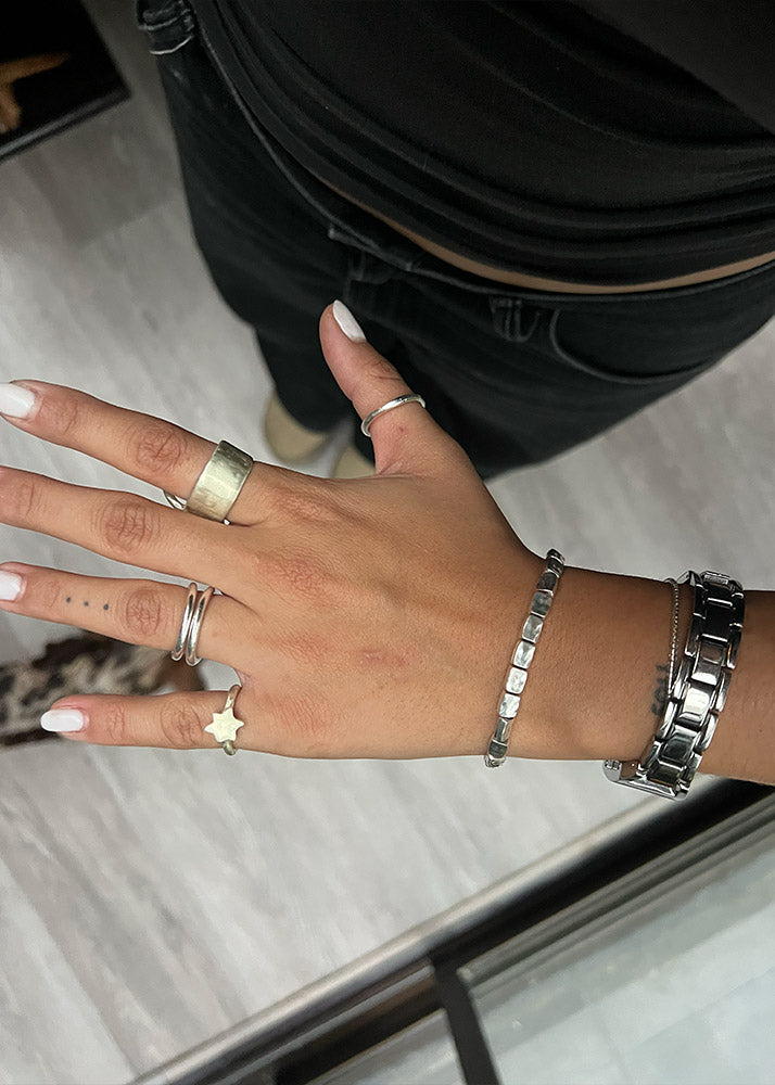 Hand with multiple silver rings and bracelets on a neutral background