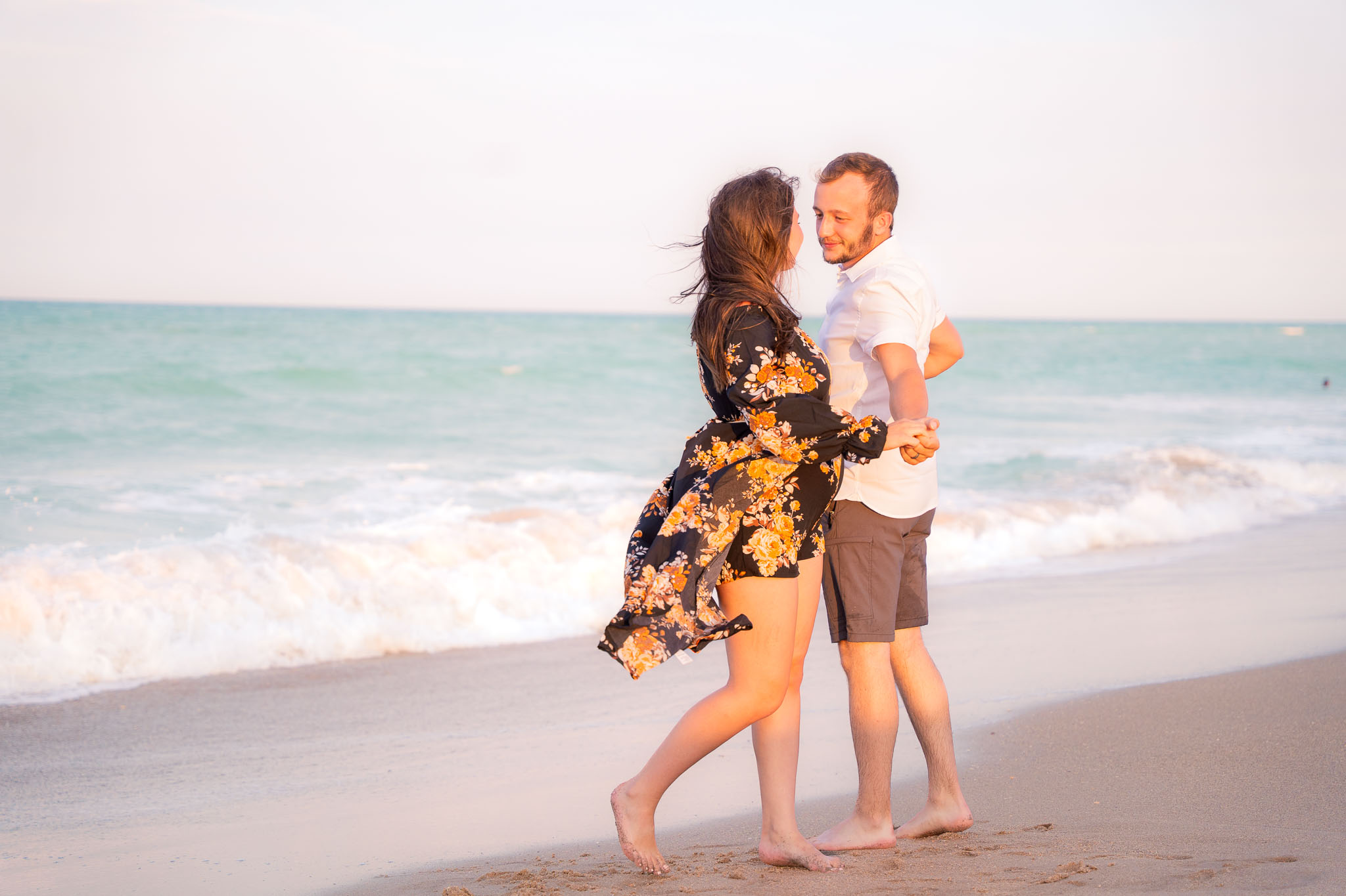  a couple gazing into each other's eyes while they hold each other's hands in front of the ocean