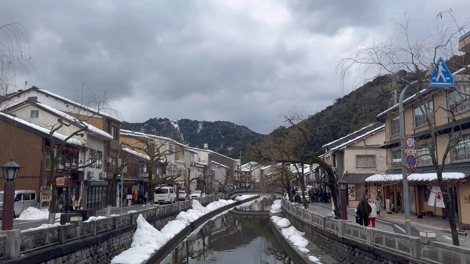 The Kinosaki canal banked with deep snow, inns and shopfronts along both sides.