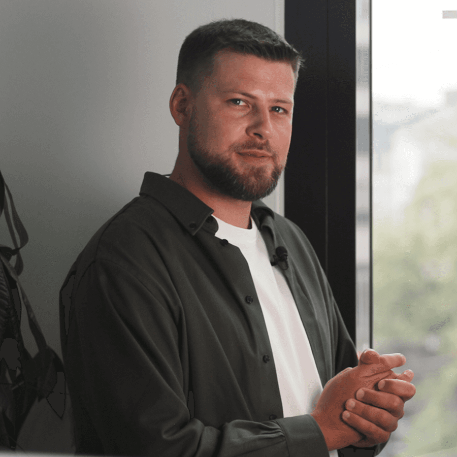 Woman with a short haircut smiling confidently, wearing a blazer and standing in warm natural light with modern architecture behind her.