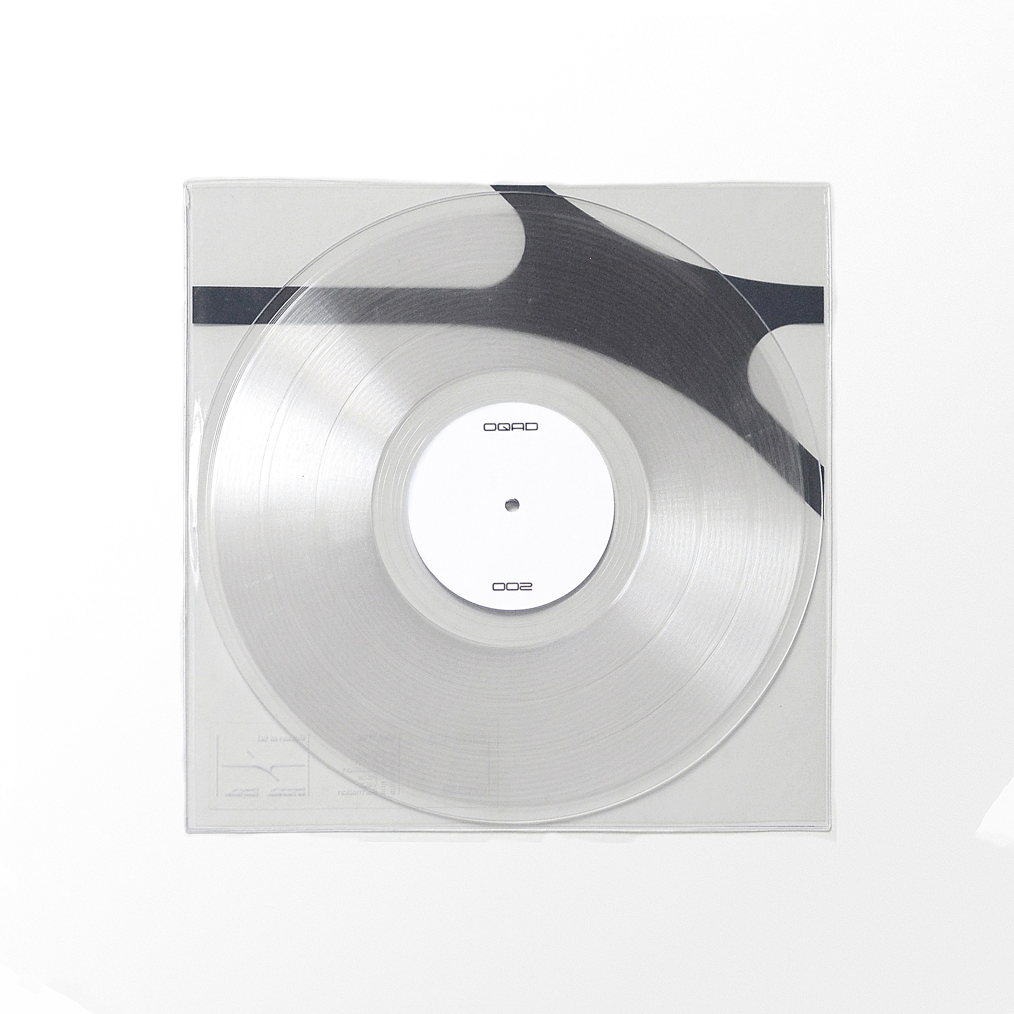 Overhead clear OQAD 002 vinyl in sleeve with plain white centre label and a subtle dark graphic behind it