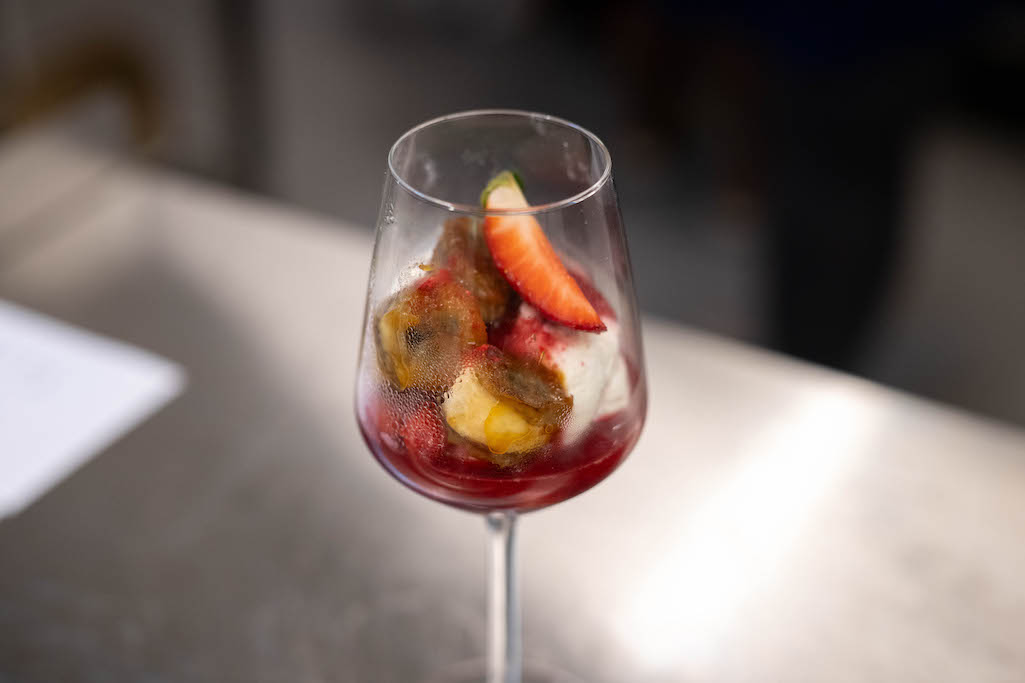 a glass of cocktail with a slime orange fruit