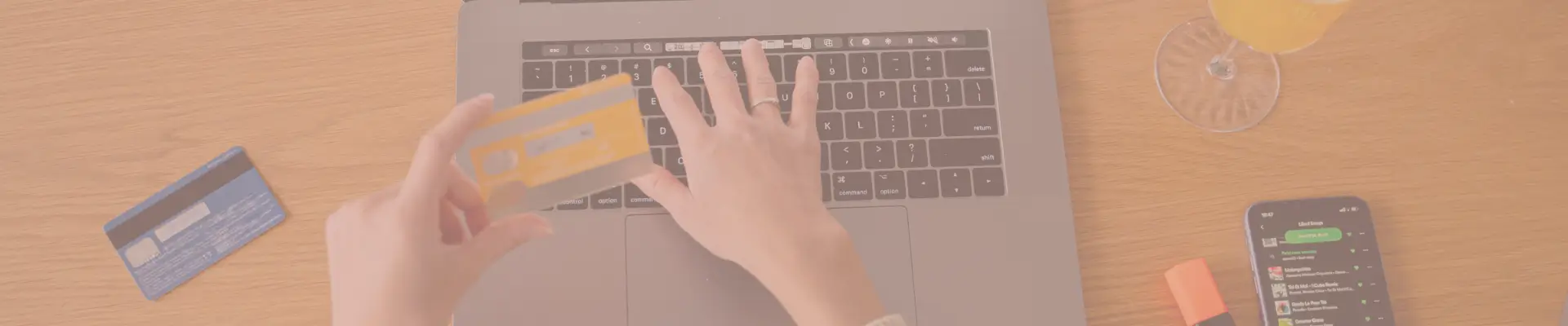 Person entering credit card details on a laptop keyboard with another card, a phone, and a drink nearby—representing a secure and efficient online checkout process.