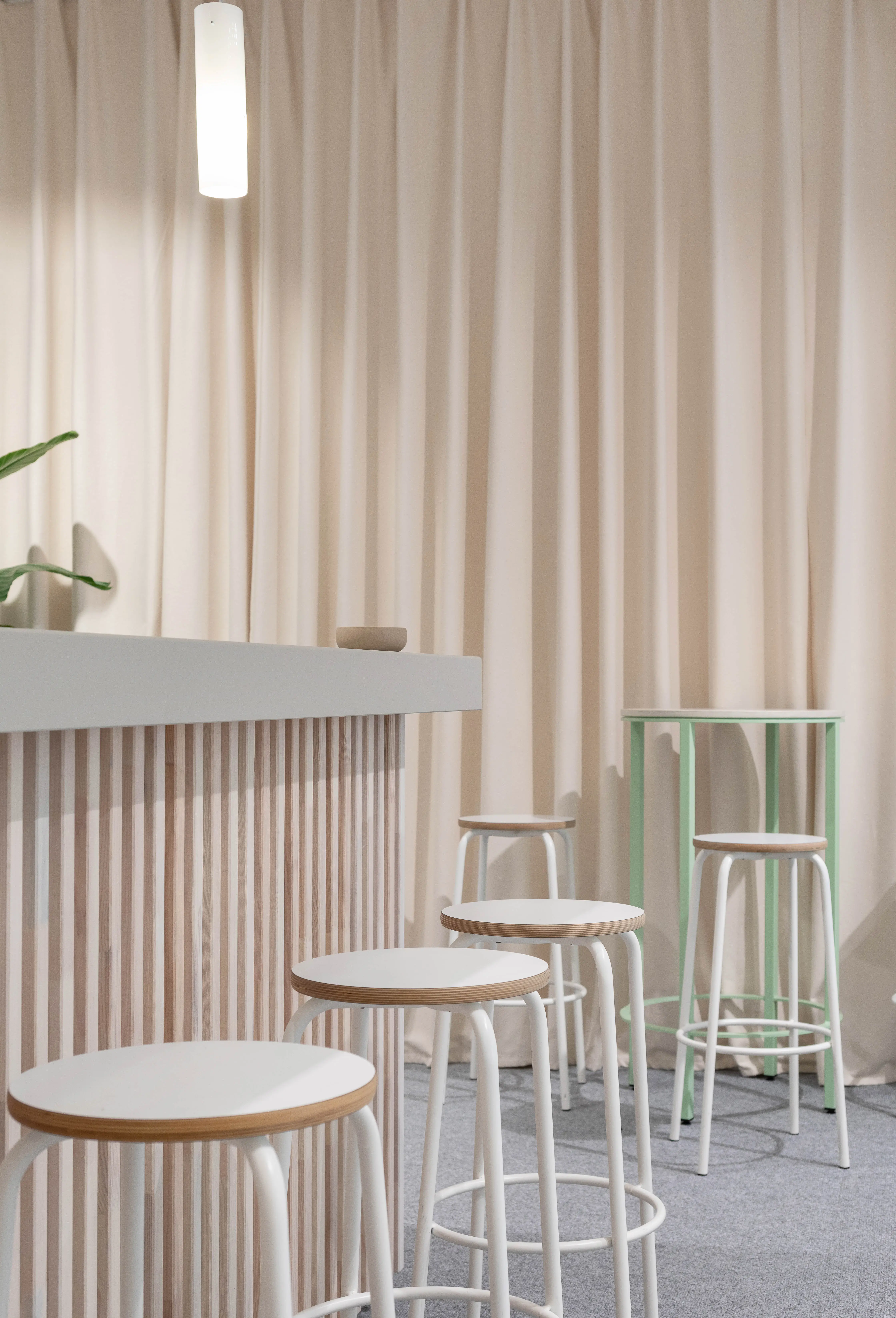 Detail of white bar stools and a mint-green high table in front of soft beige curtains in the Vossloh house.