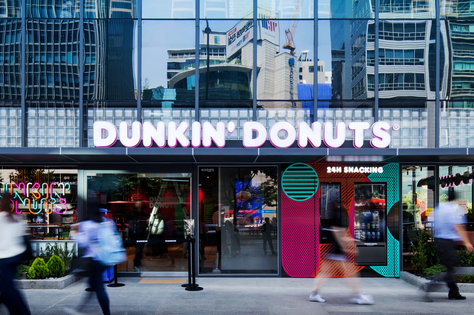 A storefront of Dunkin' Donuts with people walking by in an urban setting, showcasing modern architecture.
