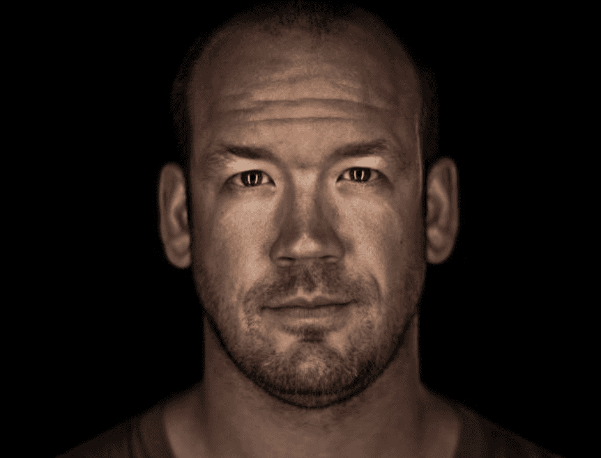 Director Zach Guerra, known for his expertise in comedy, sports, and virtual production, is captured in a dramatic close-up portrait against a black background. His direct gaze, strong features, and rugged texture convey intensity and focus, evoking the spirit of high-performance storytelling.