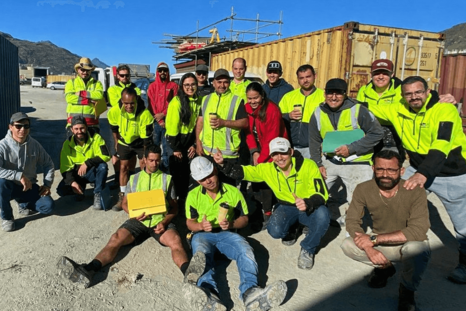 Portrait of three smiling people standing side by side against a neutral background — two men wearing black and grey t-shirts and a woman in a black zip-up hoodie.
