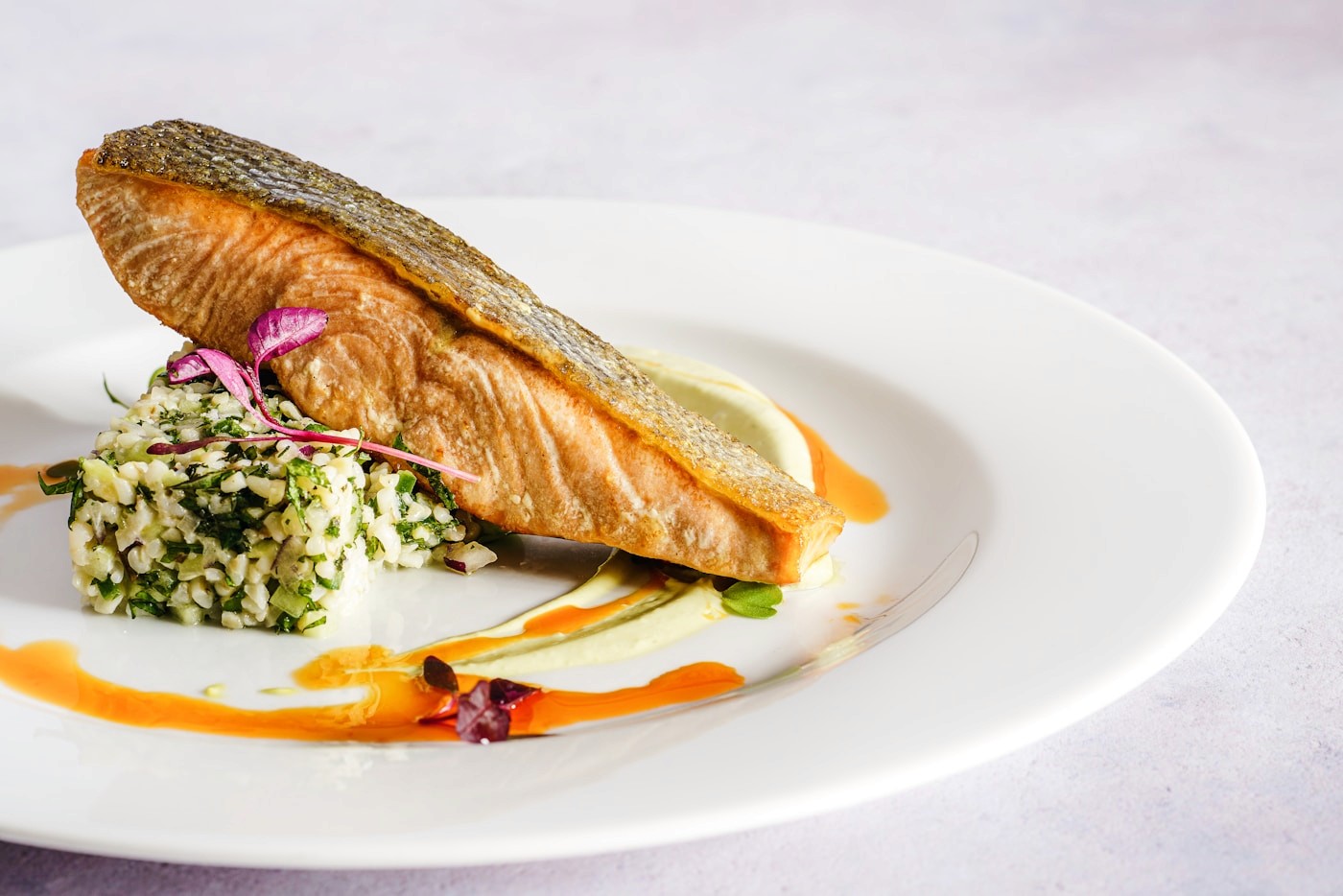 A cooked salmon fillet served with a herbed rice cake on a white plate, an example of omega-3-rich unsaturated fat