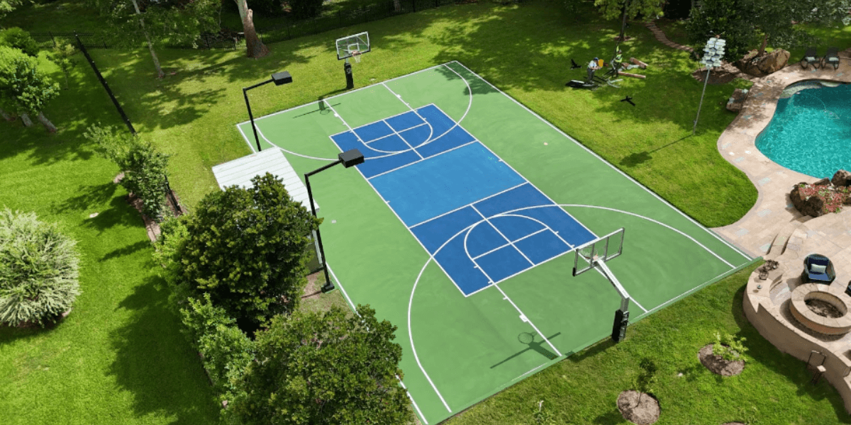 Aerial view of professional multi-sport pickleball and basketball court with green and blue surfaces built by Texas court builders BuildMyCourts in Houston residential backyard with pool