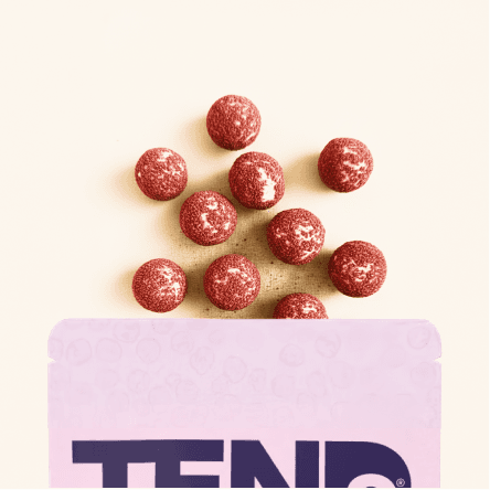 Small round coated dog snacks arranged above TENDS Superfood Pops packaging on a neutral background