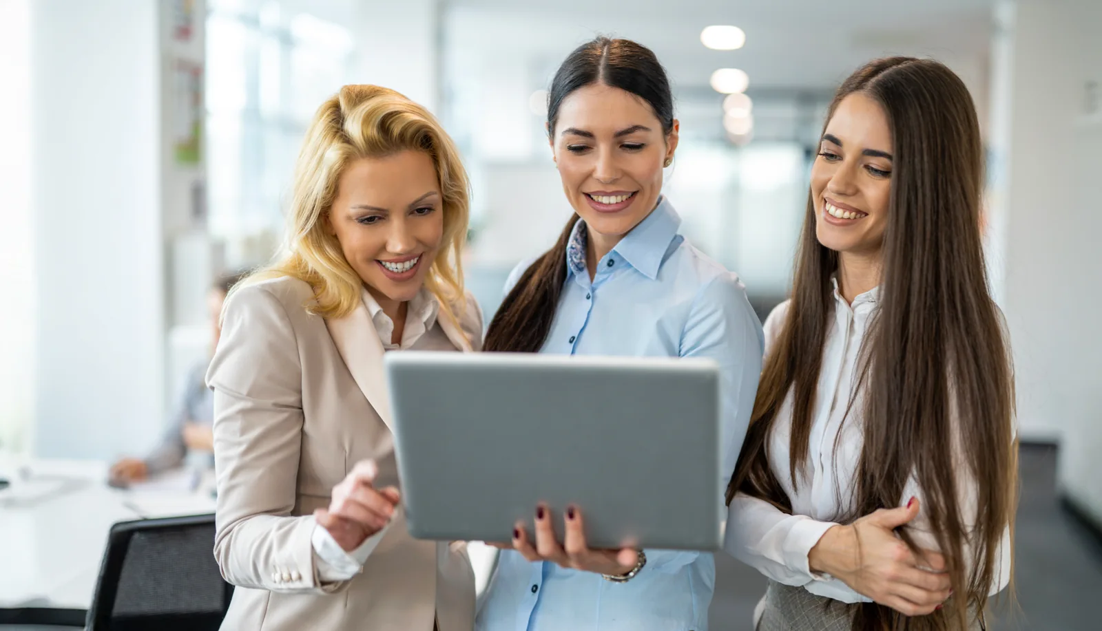 Three smiling colleagues reviewing a laptop together in a bright office
