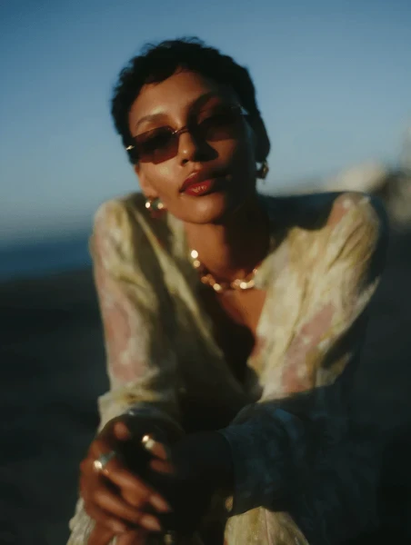 Out-of-focus close-up of a person wearing large gold earrings and a gold necklace with a yellow top.