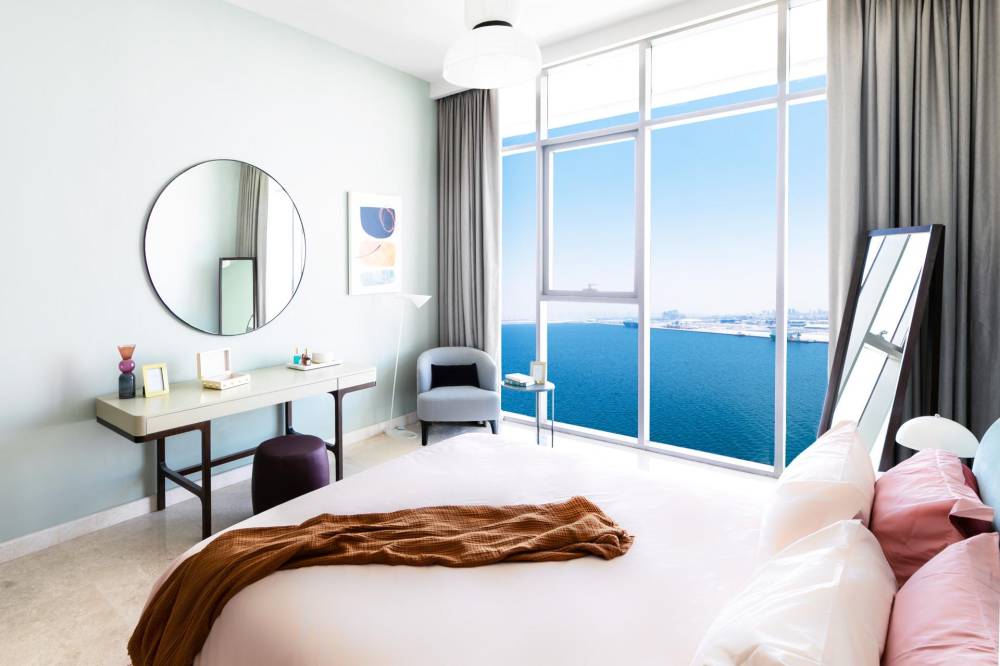 A spacious bedroom featuring a large bed and an expansive mirror, designed for comfort and style at Anwa Omniyat Maritime City.