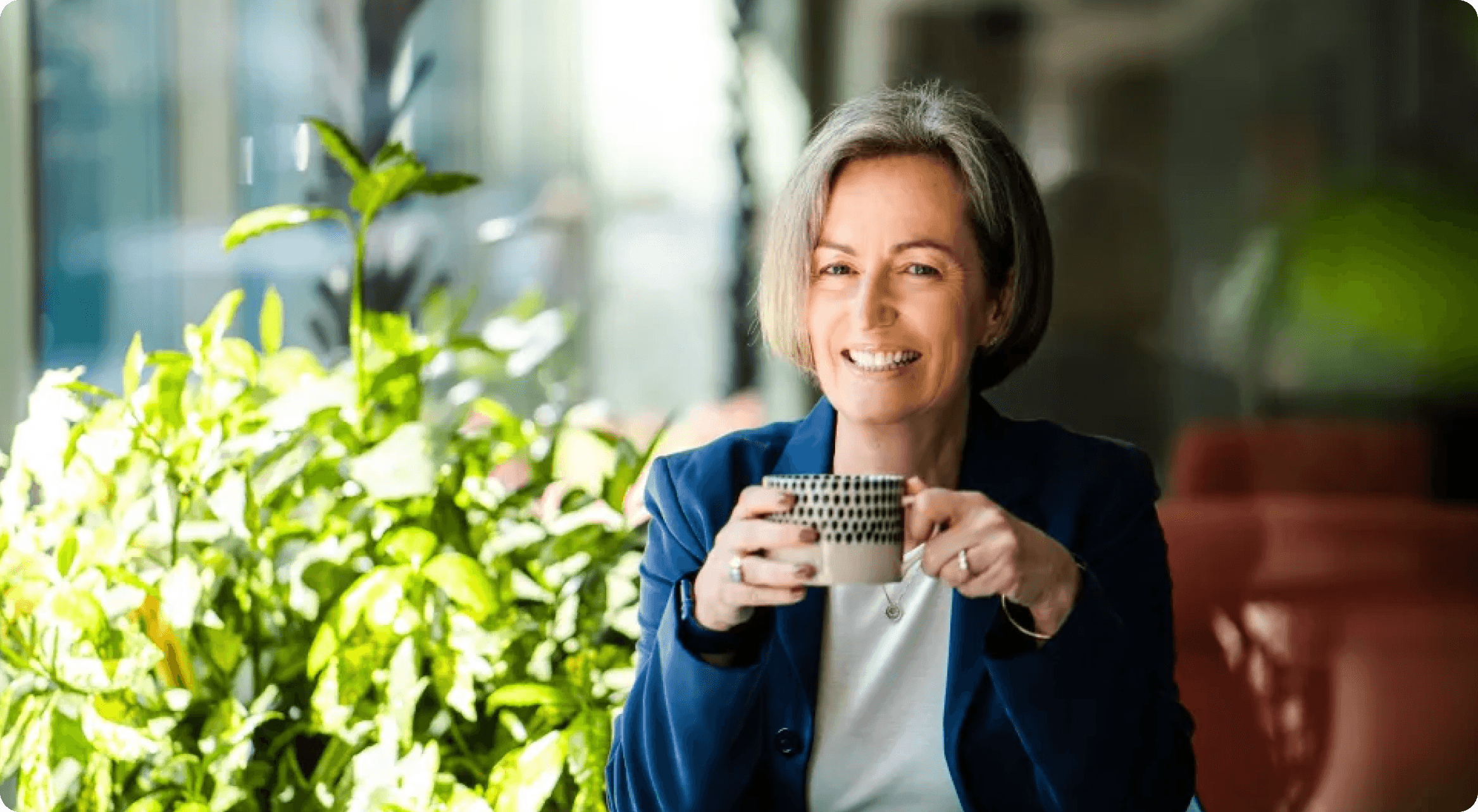 Kate sitting with a tea cup in hand with some greenery in the background