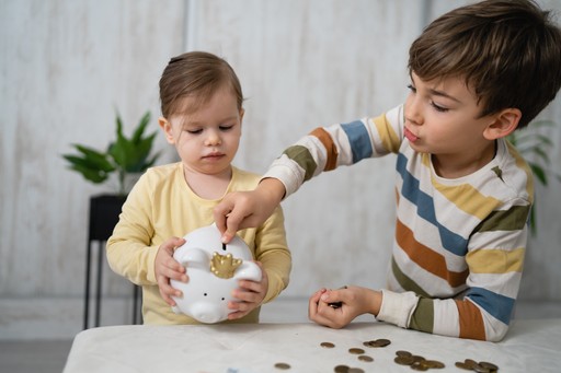 Two young children are pouring colorful materials into a container, engaged in a creative activity indoors.
