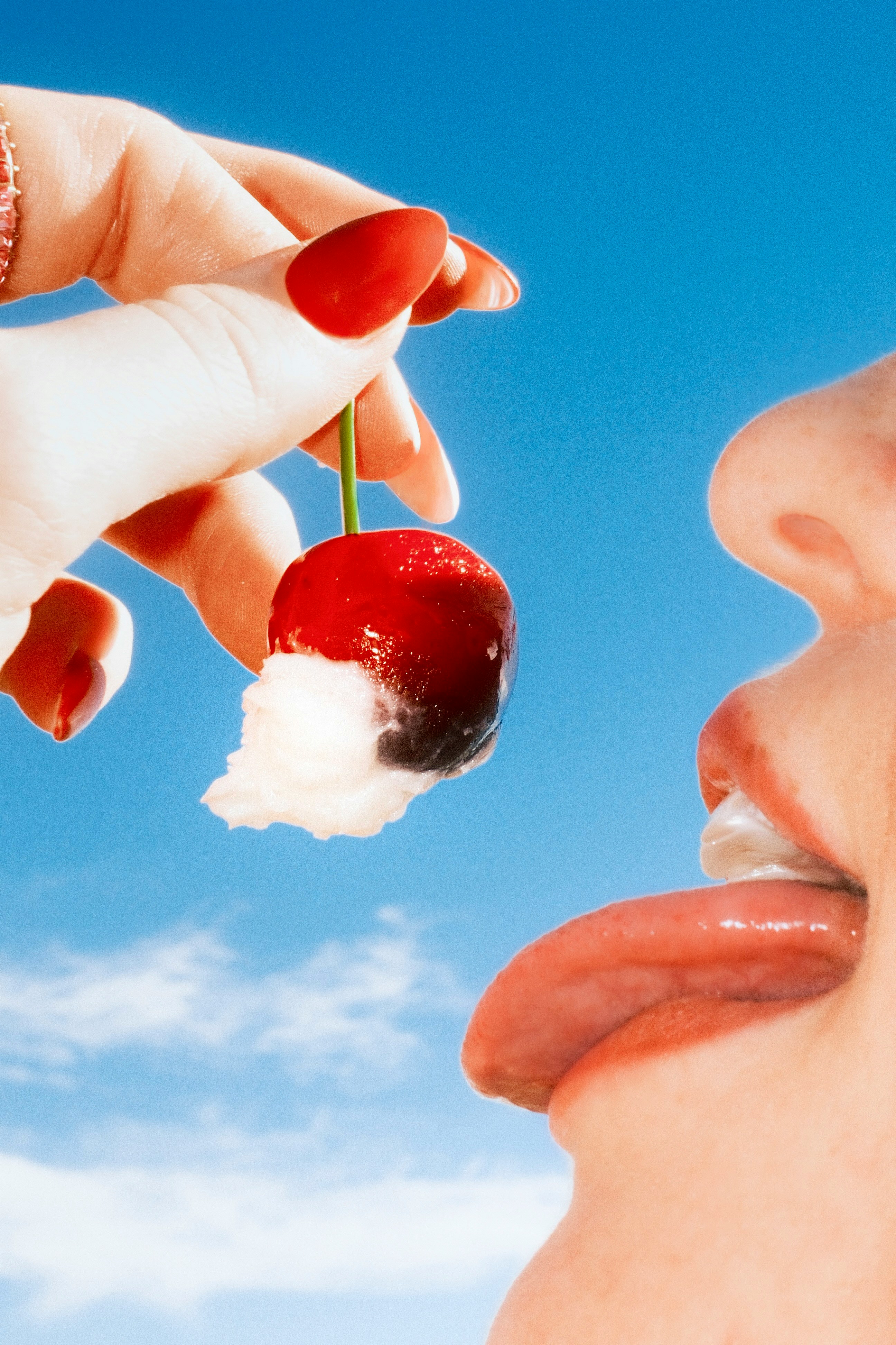 Hand offering cherry to mouth against blue sky