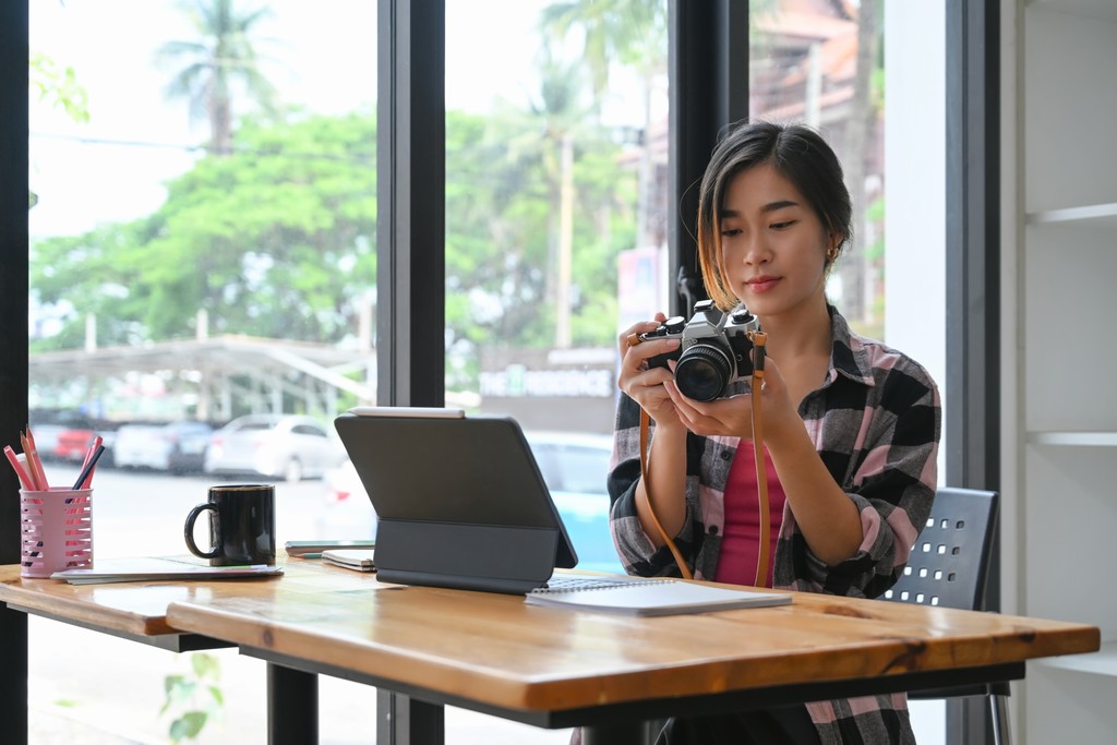 Photographer reviewing camera at desk with tablet and coffee