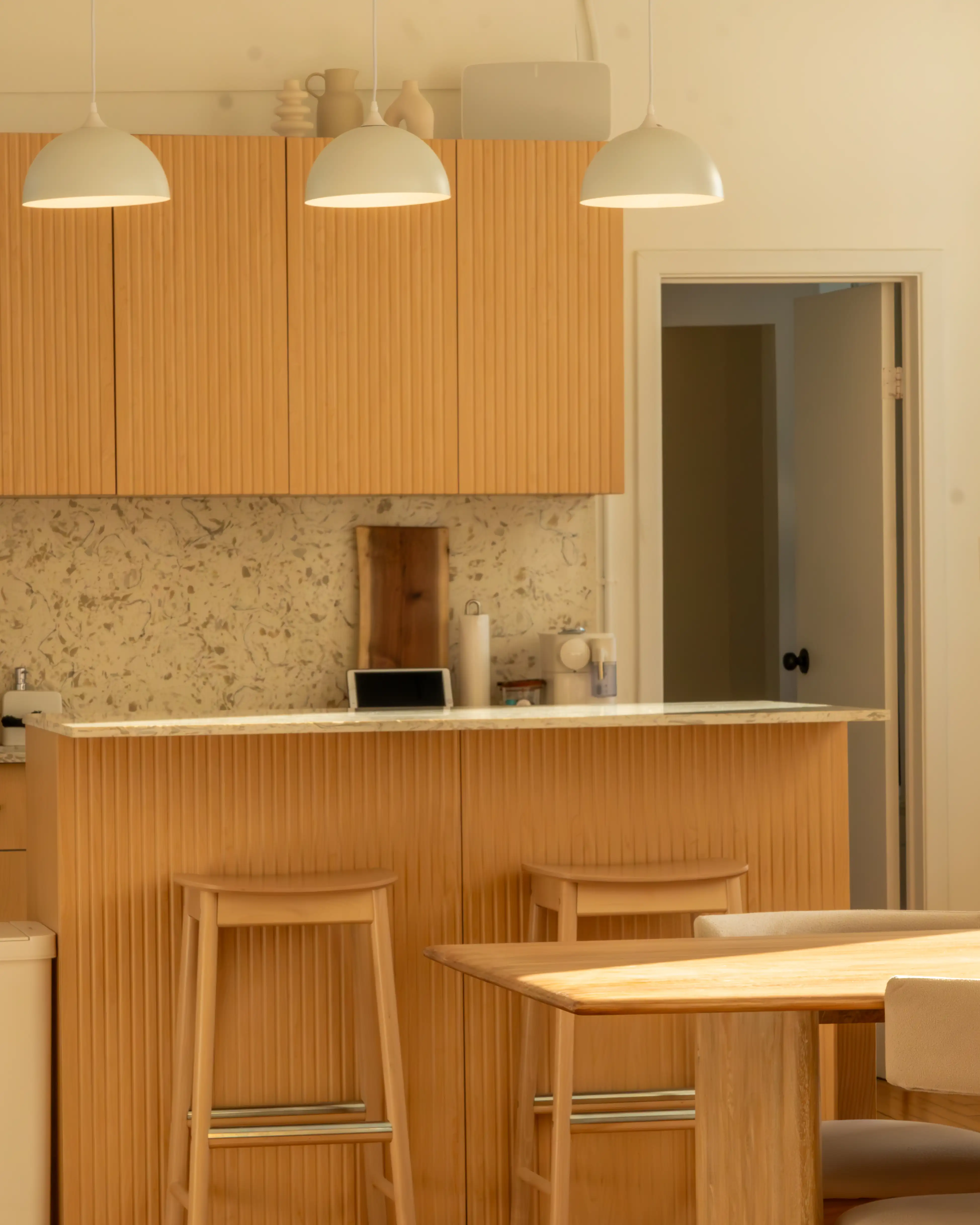 “Node Studio’s modern semi-equipped kitchen, featuring warm wooden cabinetry, sleek bar stools, and soft pendant lighting, creating a functional and minimalist environment for content creation and culinary projects