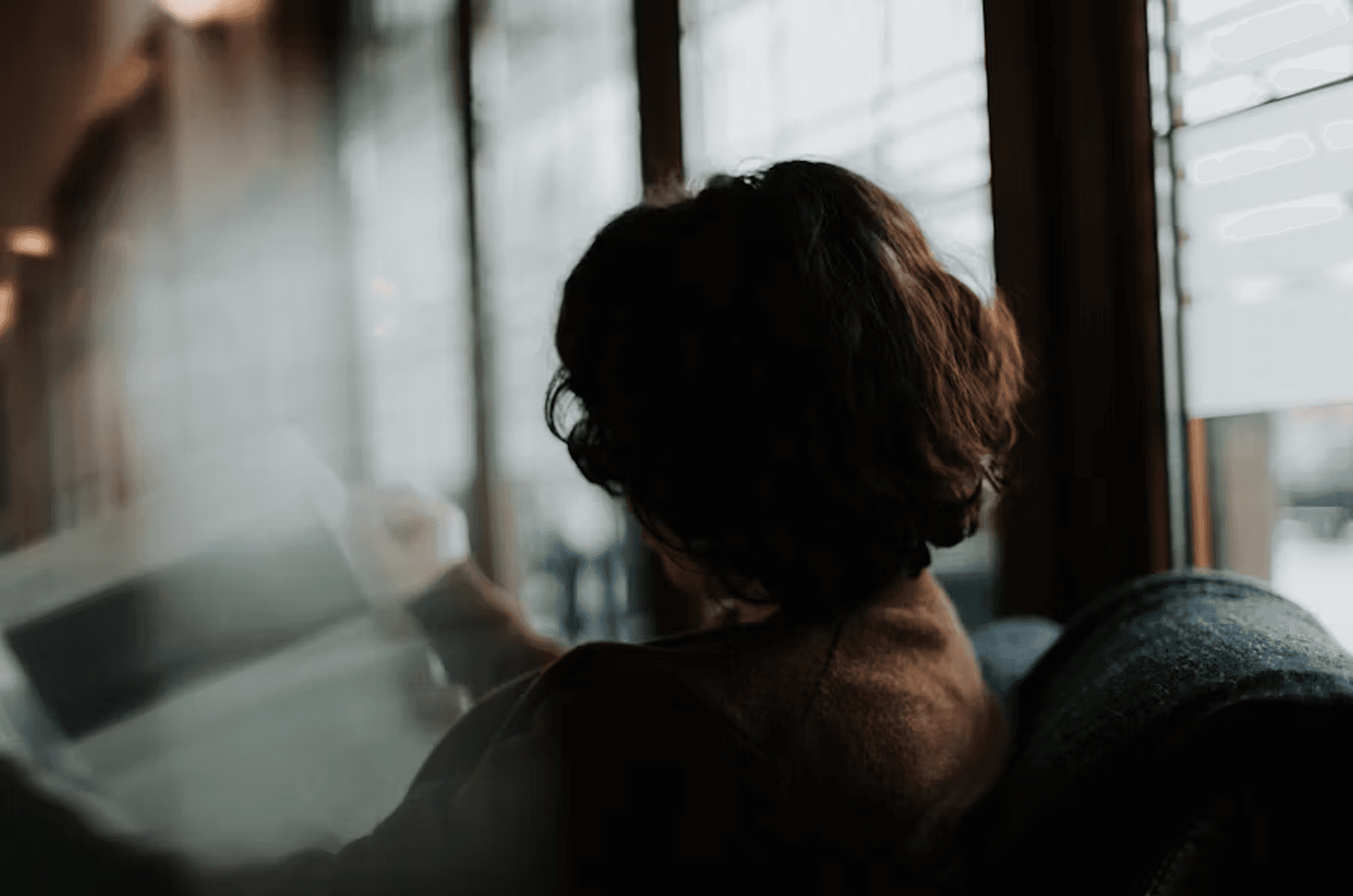 A person sitting by a window, seen from behind in low light, symbolizing Salesforce vs HubSpot for LinkedIn Ads integration.
