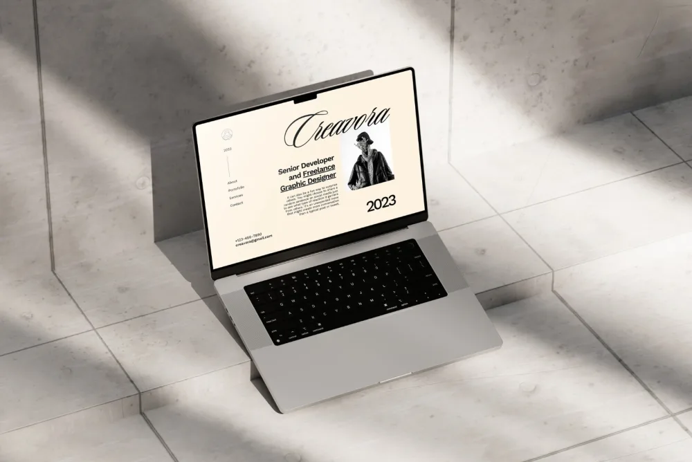 Open MacBook Pro placed on a light concrete surface, displaying a beige-toned portfolio website design with elegant typography, a black-and-white portrait, and soft natural light shadows.