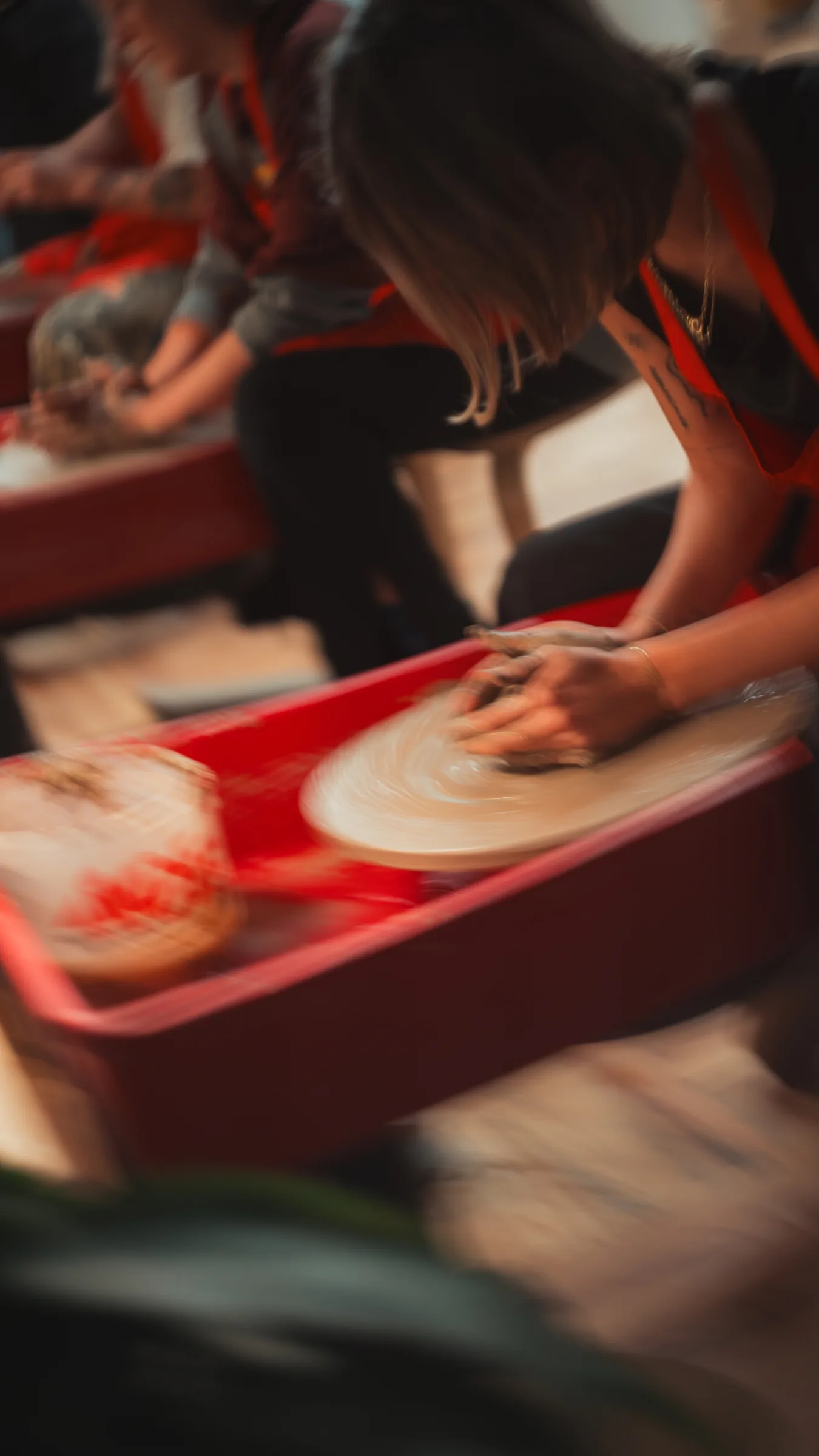 Member's hands centering clay on a red pottery wheel at Kinship Studio